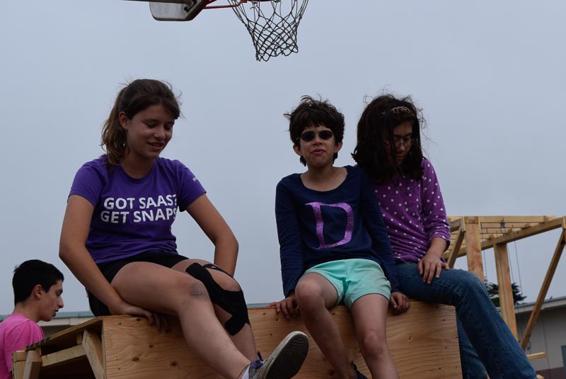 Hannah, Odyssey, and Kira have a conversation sitting on the Panda box/rock climbing wall.