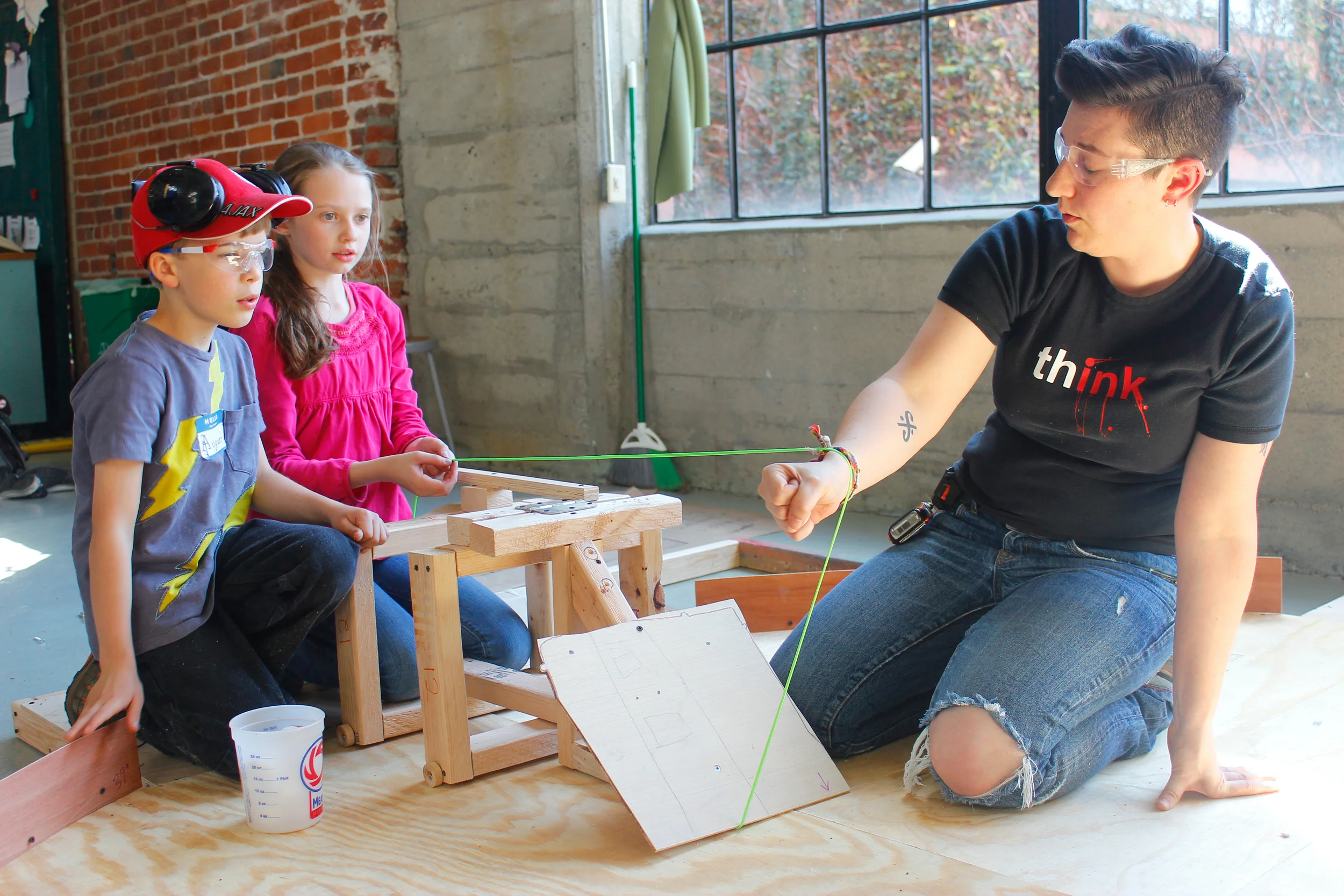Freya, August, and Amanda try to figure out where to place a pulley on a giant version of the board game "Hungry Hungry Hippos."