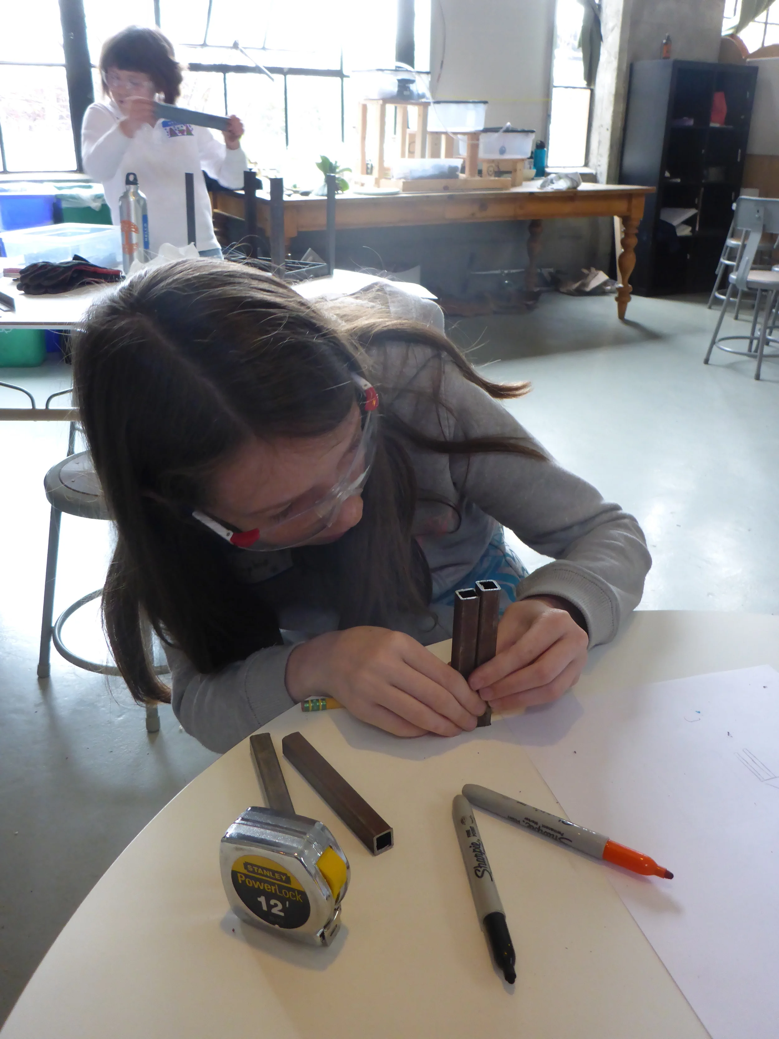Sophie measures some pieces of 1/2" square tube to see if they will work for her table.