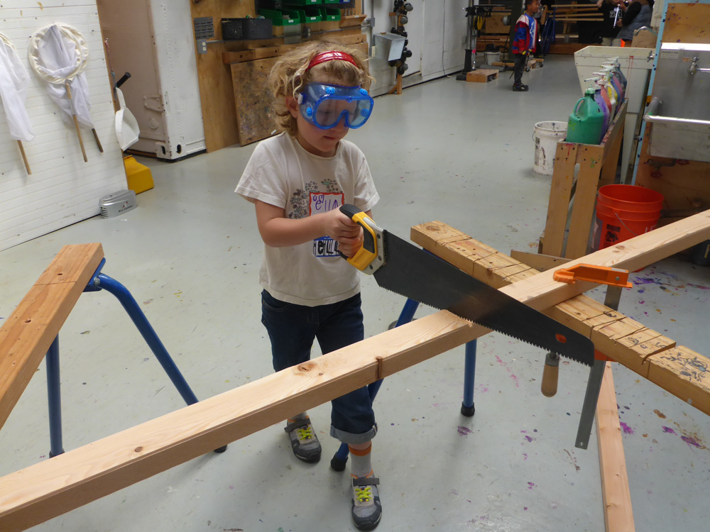 Ella uses a hand saw to cut a specialty piece.