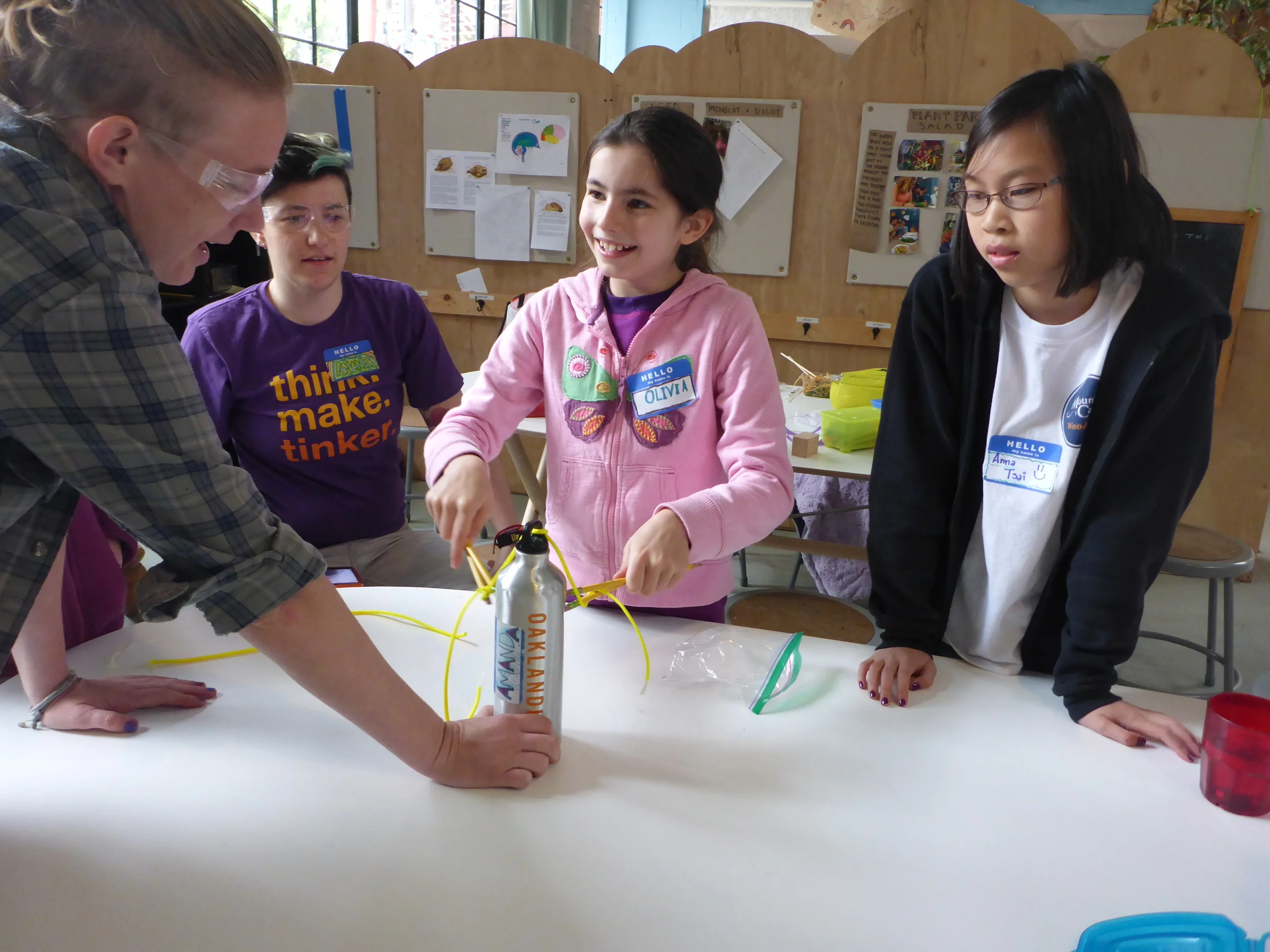 Lindsay, Amanda, Olivia and Anna try to tie a length of paracord around a water bottle just using pencils as chopsticks.