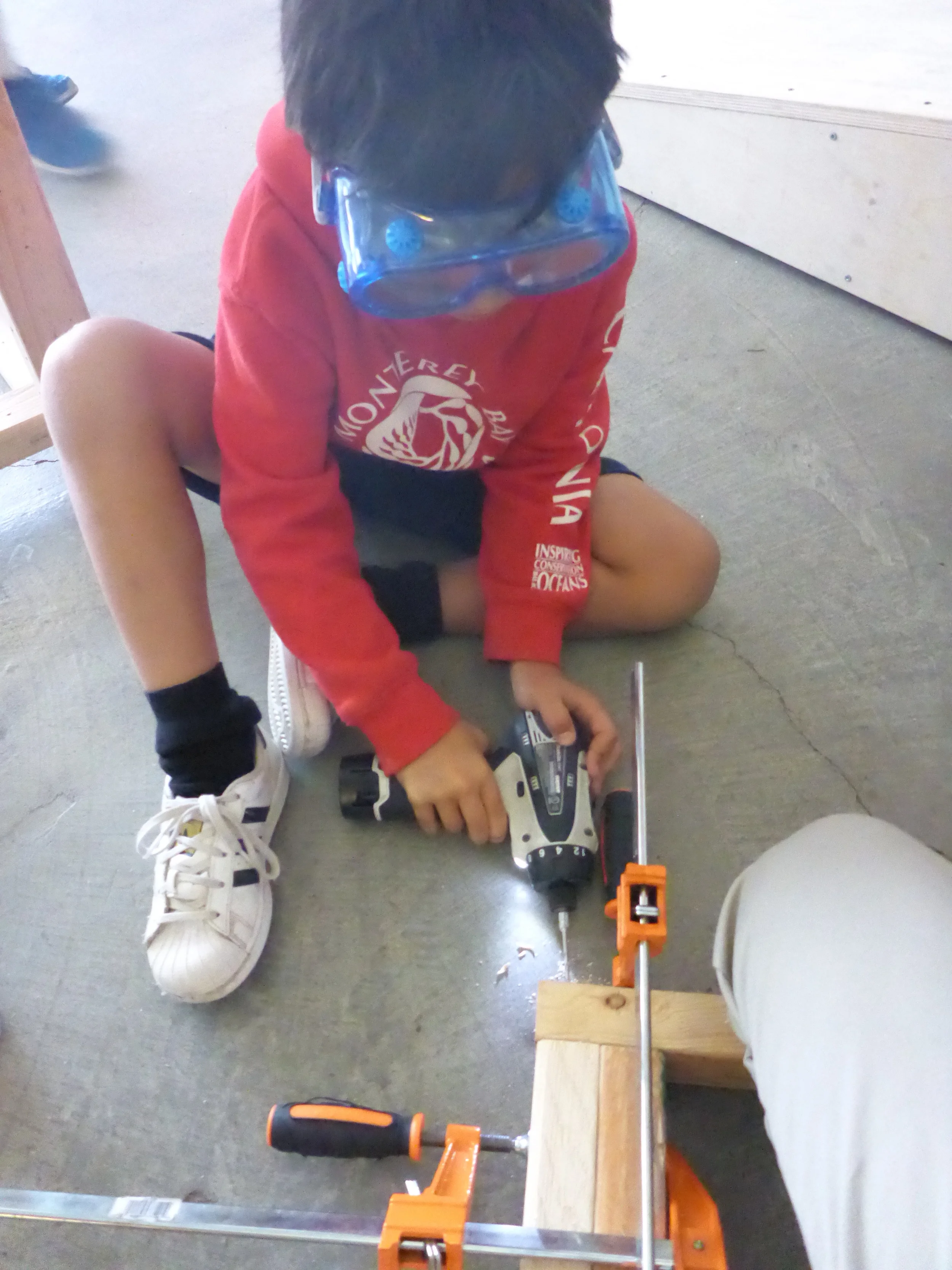 Ryo takes turns drilling holes into the bird head frame for his partner to follow behind and drive in screws.