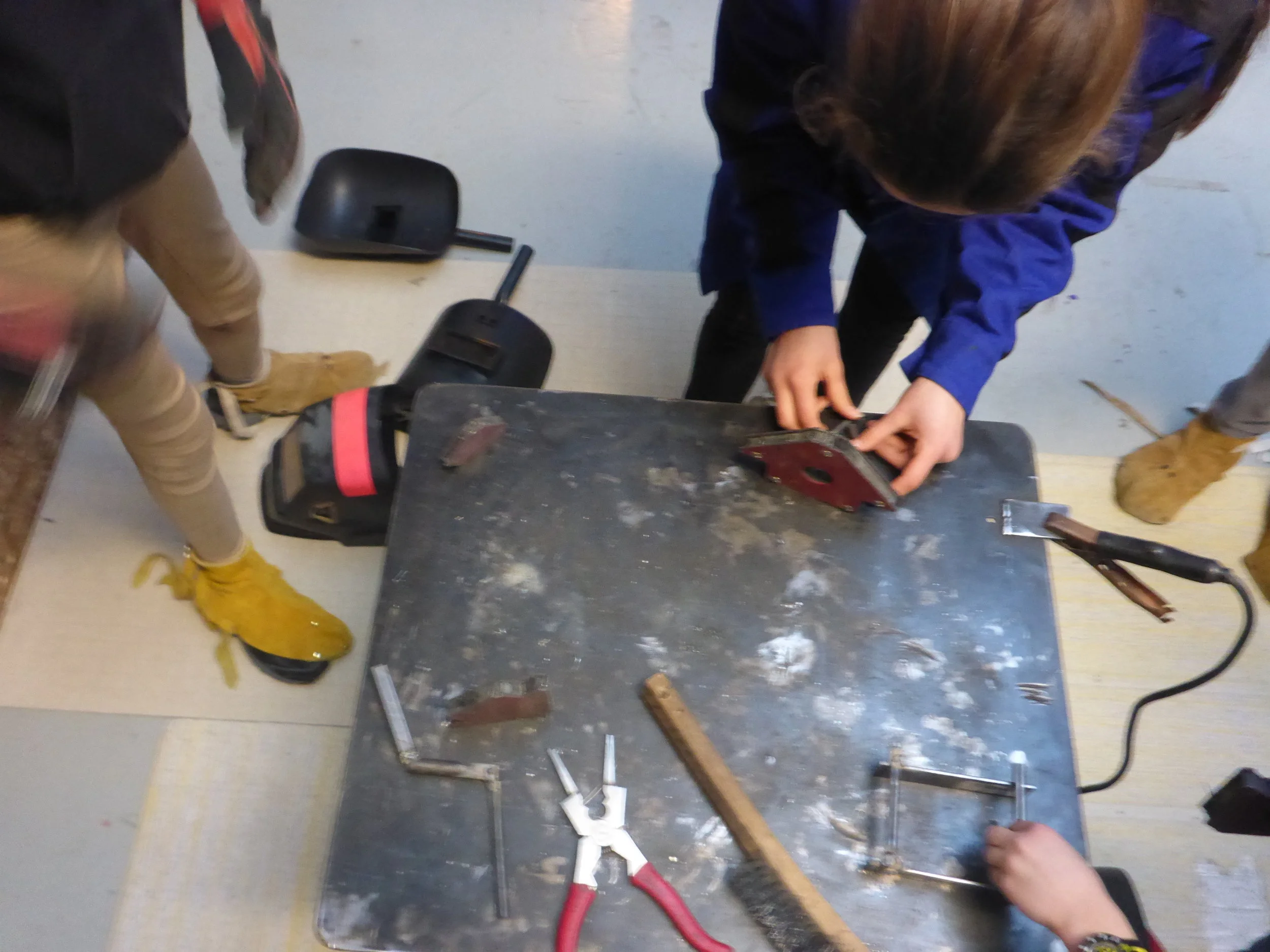 Many busy hands setup their welds on the table, so that the welding gun can move quickly from one person to the next. 