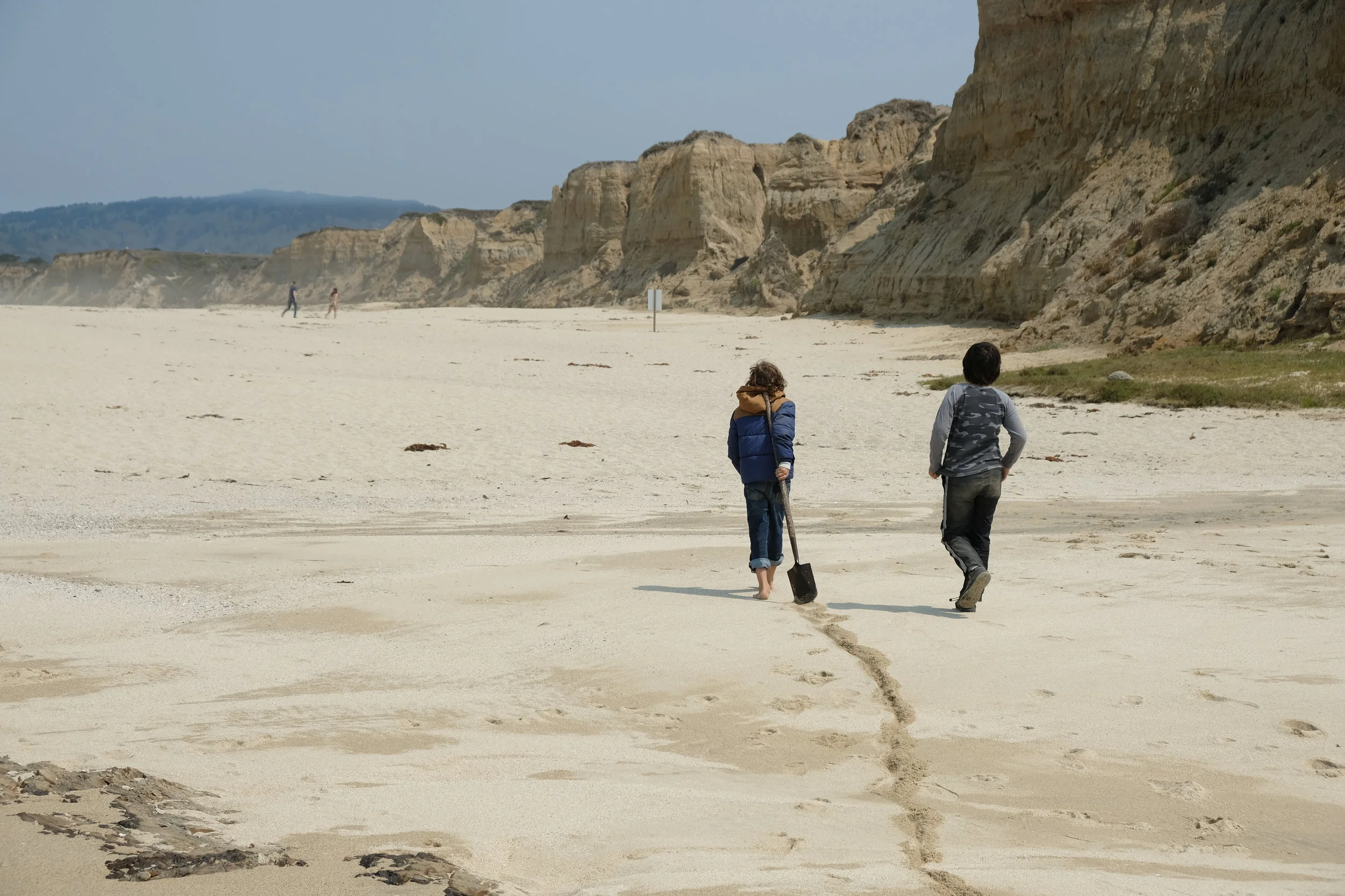 Brody and Alex walk with their shovel down the beach.