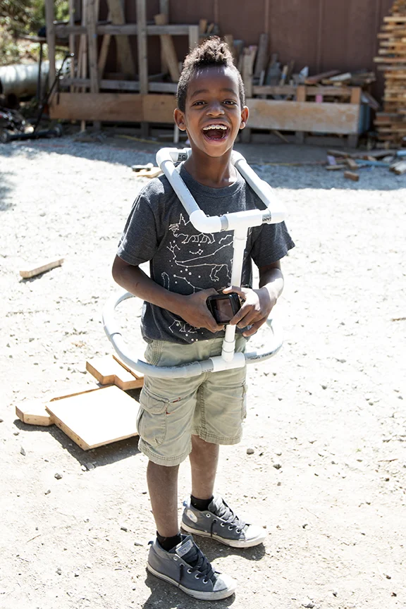 Junior Tinkerer, Adane, laughs while trying on the Mini Mech Suit he built to fit his frame.