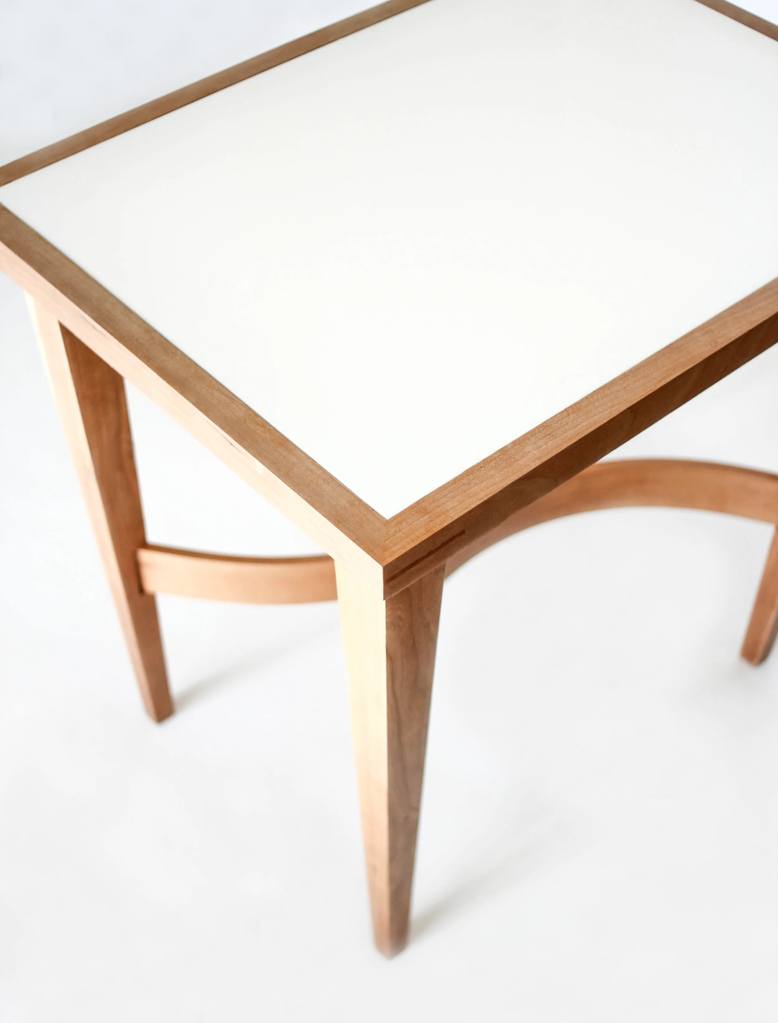Made of solid Cherry, this side table was made while studying bent wood lamination. An opaque, plexiglass top sits inside the frame, accented with Walnut splines on all four corners. Playing also with scale, the tapered legs give the table its exagerated sense of height.