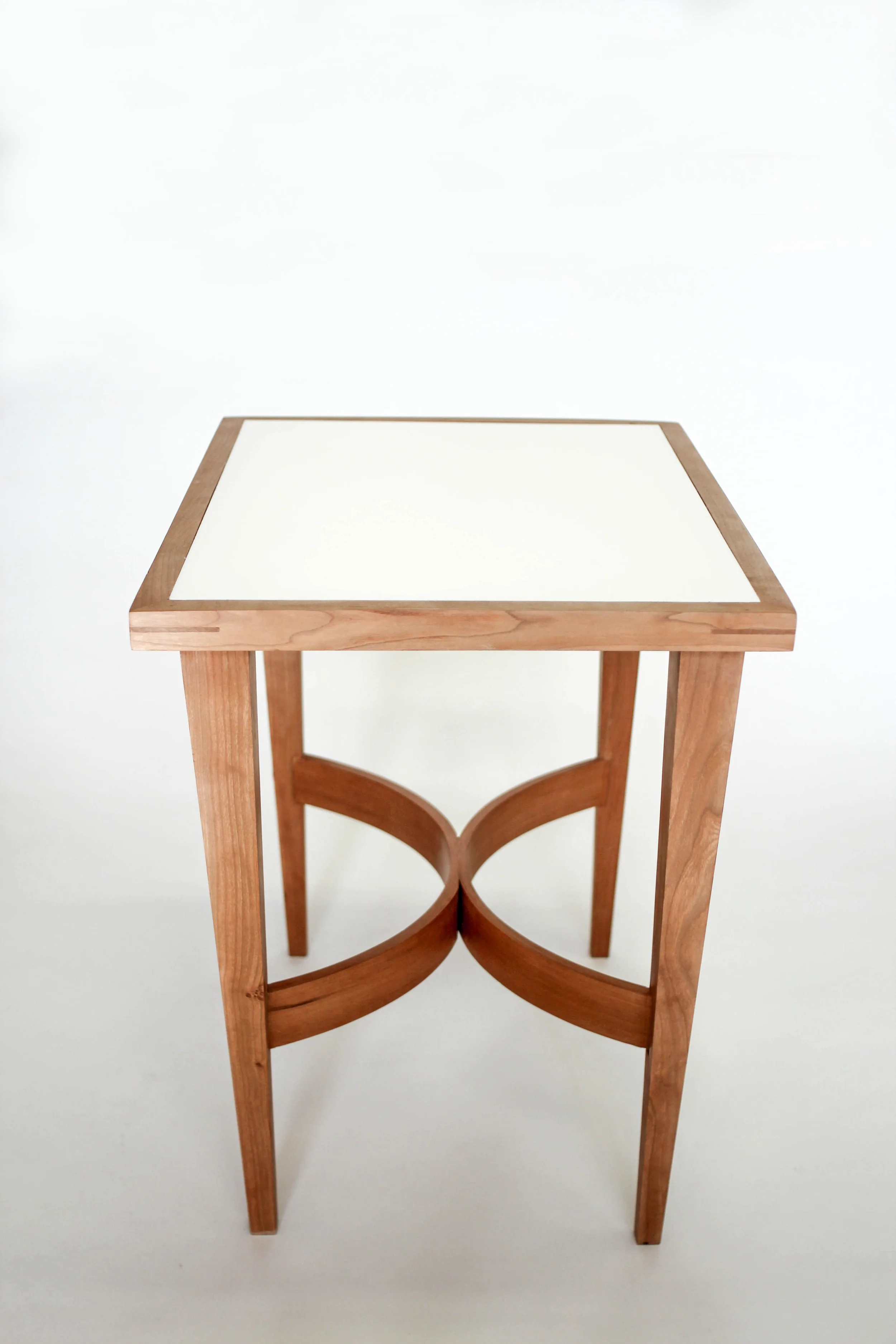 Made of solid Cherry, this side table was made while studying bent wood lamination. An opaque, plexiglass top sits inside the frame, accented with Walnut splines on all four corners. Playing also with scale, the tapered legs give the table its exagerated sense of height.