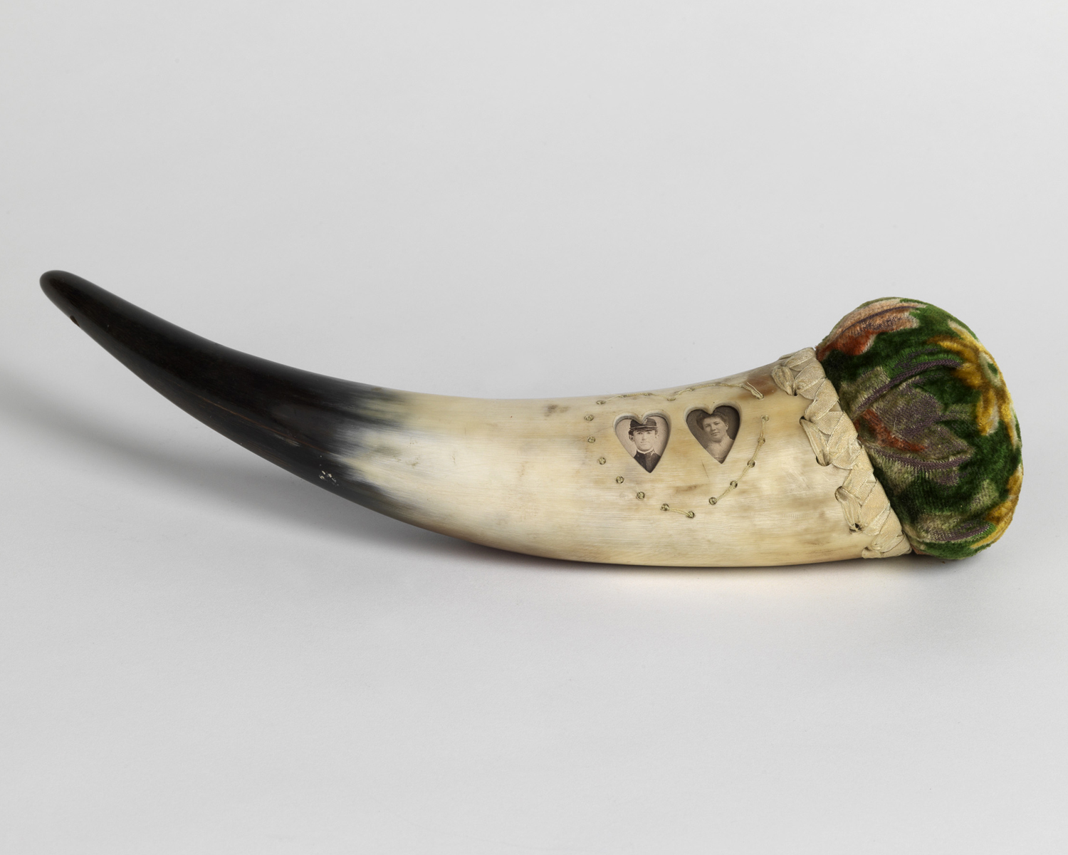    Horn with green velvet pin cushion inset with heart-shaped photographs of a man and wife.&nbsp; 1890s   