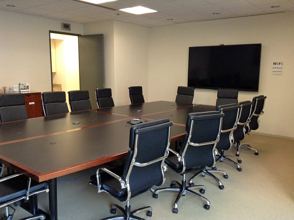 A long conference table with chairs around it. A flatscreen tv hangs on the wall at the head of the table.