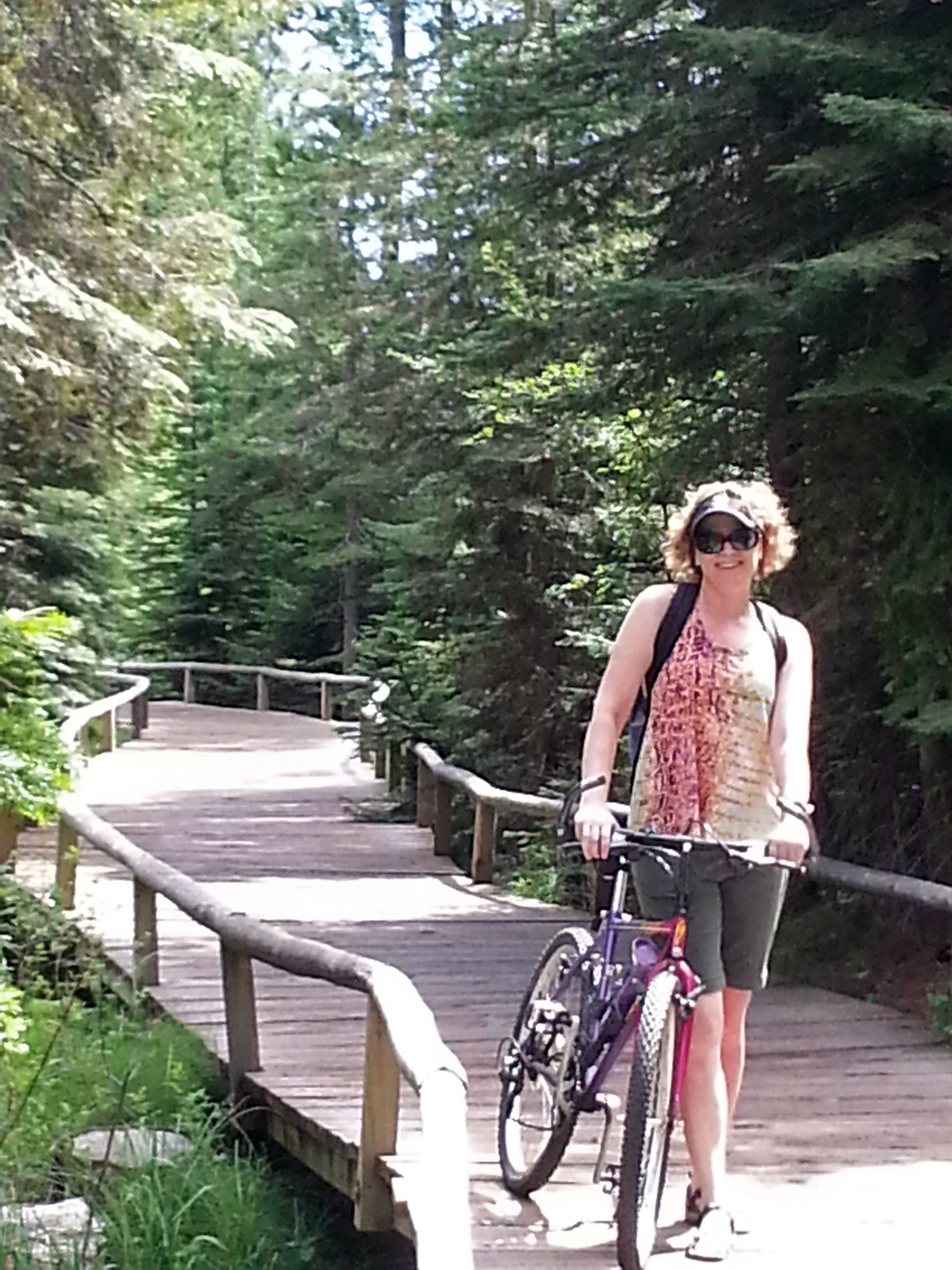 Renée with a bike on a wooden walkway surrounded by trees.