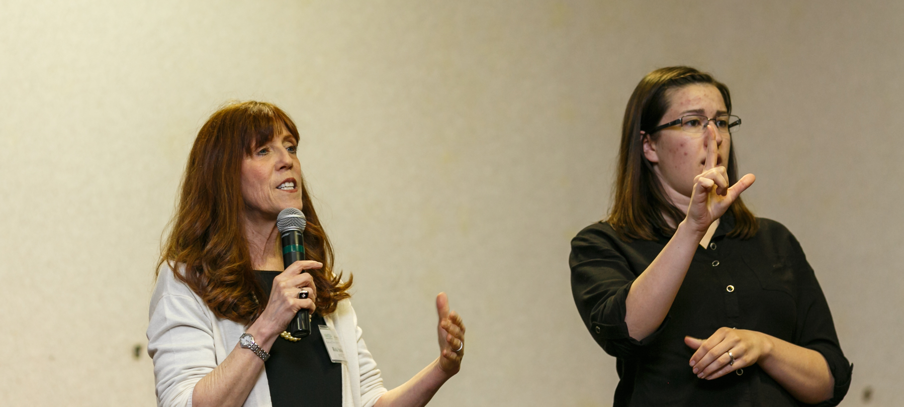 One woman speaking into a microphone, one woman signing.