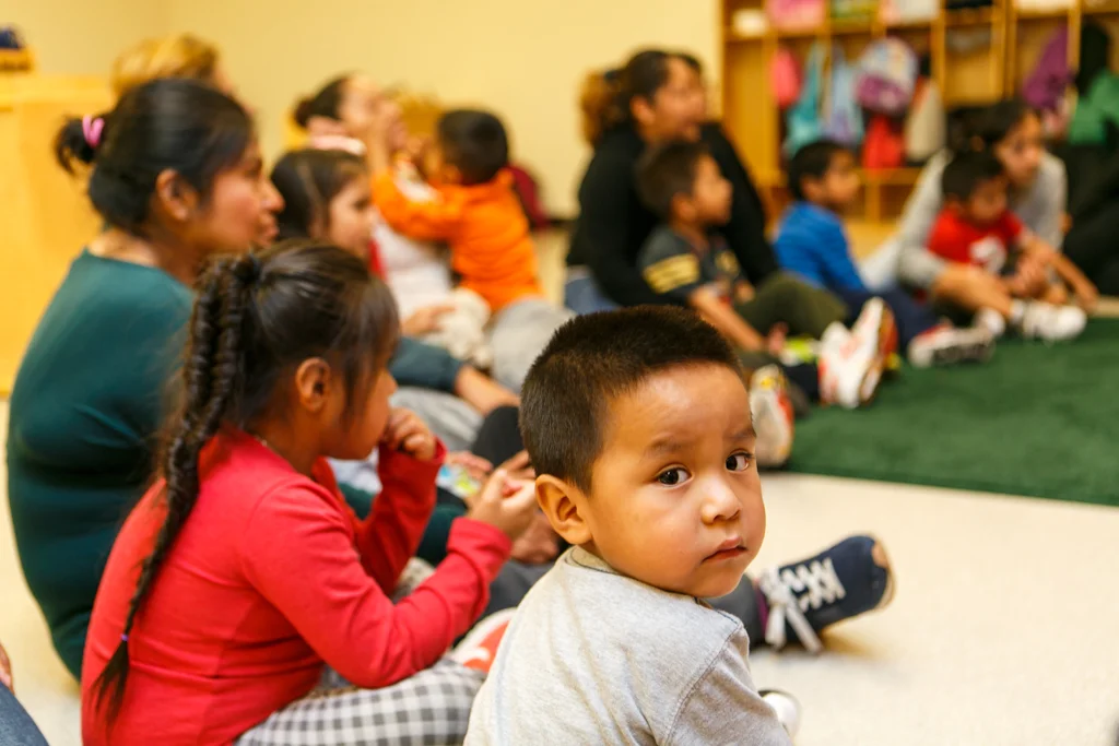 Parents and children sit in a semicircle on the floor of a classroom.