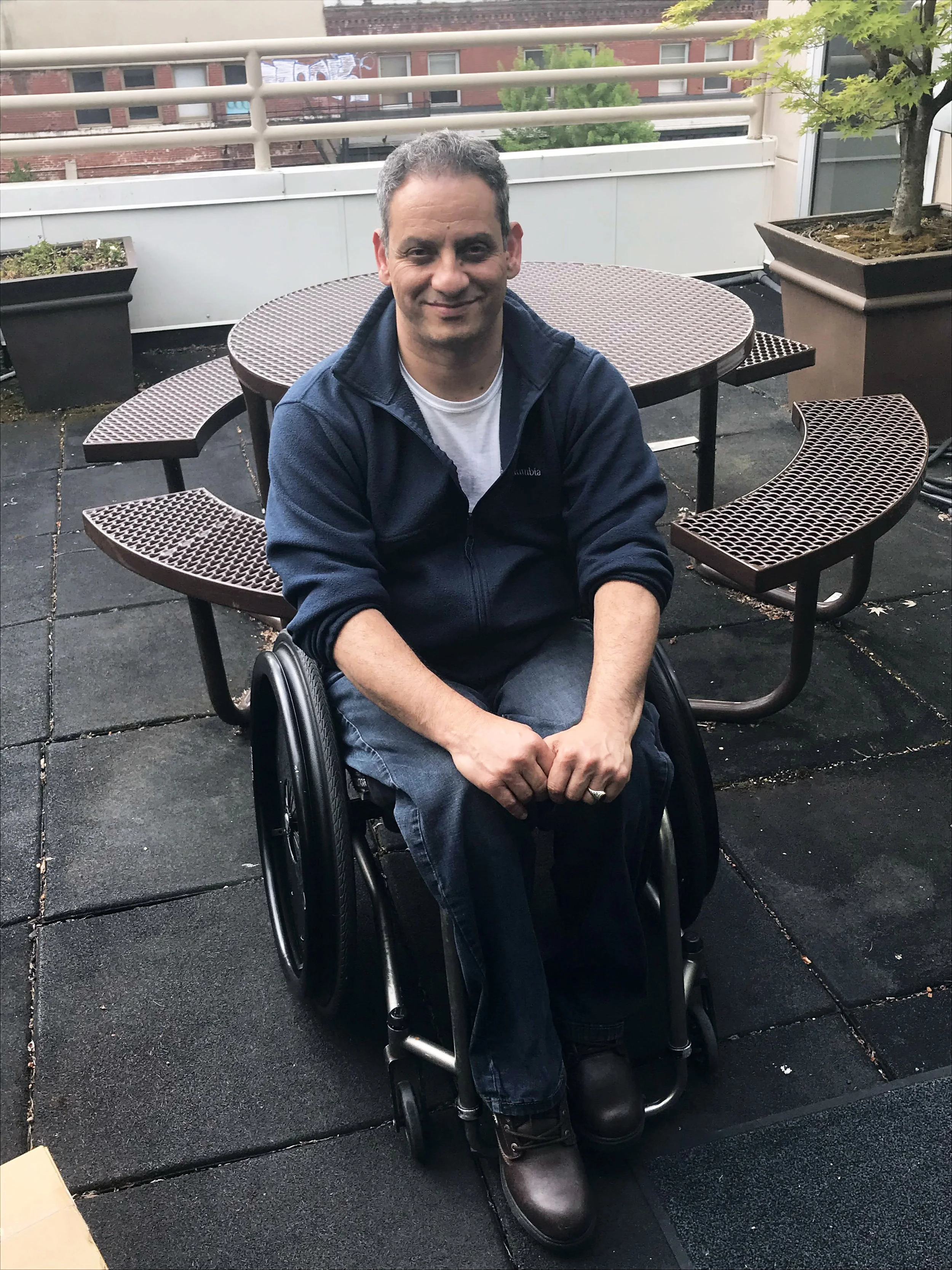 Waddah sits in a wheelchair in front of picnic table and smiles.