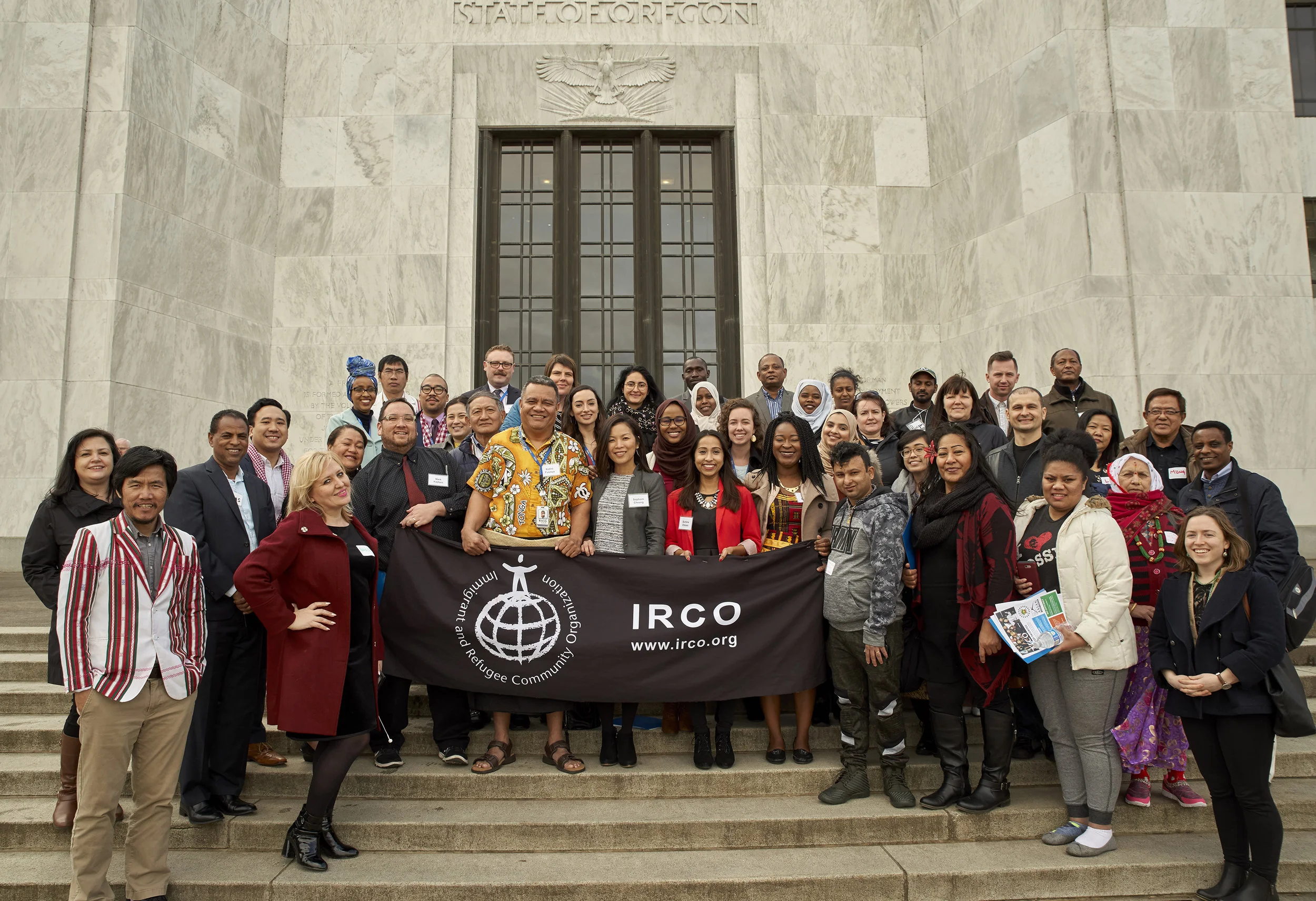 Members of the Multiethnic Advisory Group stand on the steps of Oregon's State Capitol building holding an IRCO banner.