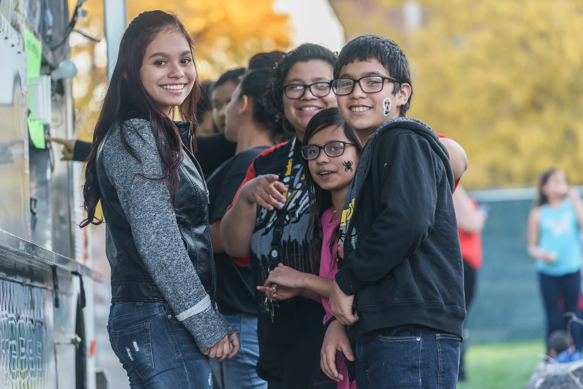Youth stand and smile beside a food cart at EUVALCREE's Day of the Dead celebration.