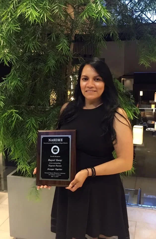 Raquel Garay smiles, holding a plaque.