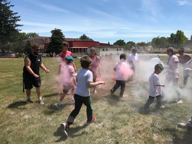 Independence Elementary students run through clouds of colored powder, tossed by adults standing on the sidelines.
