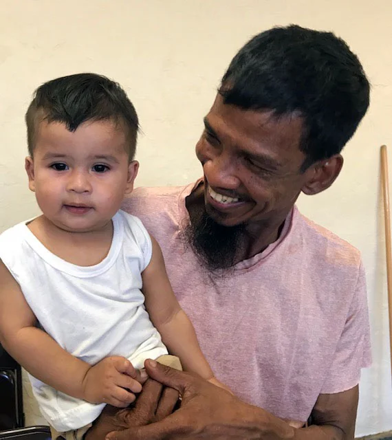 An adult holds a toddler, smiling at them.