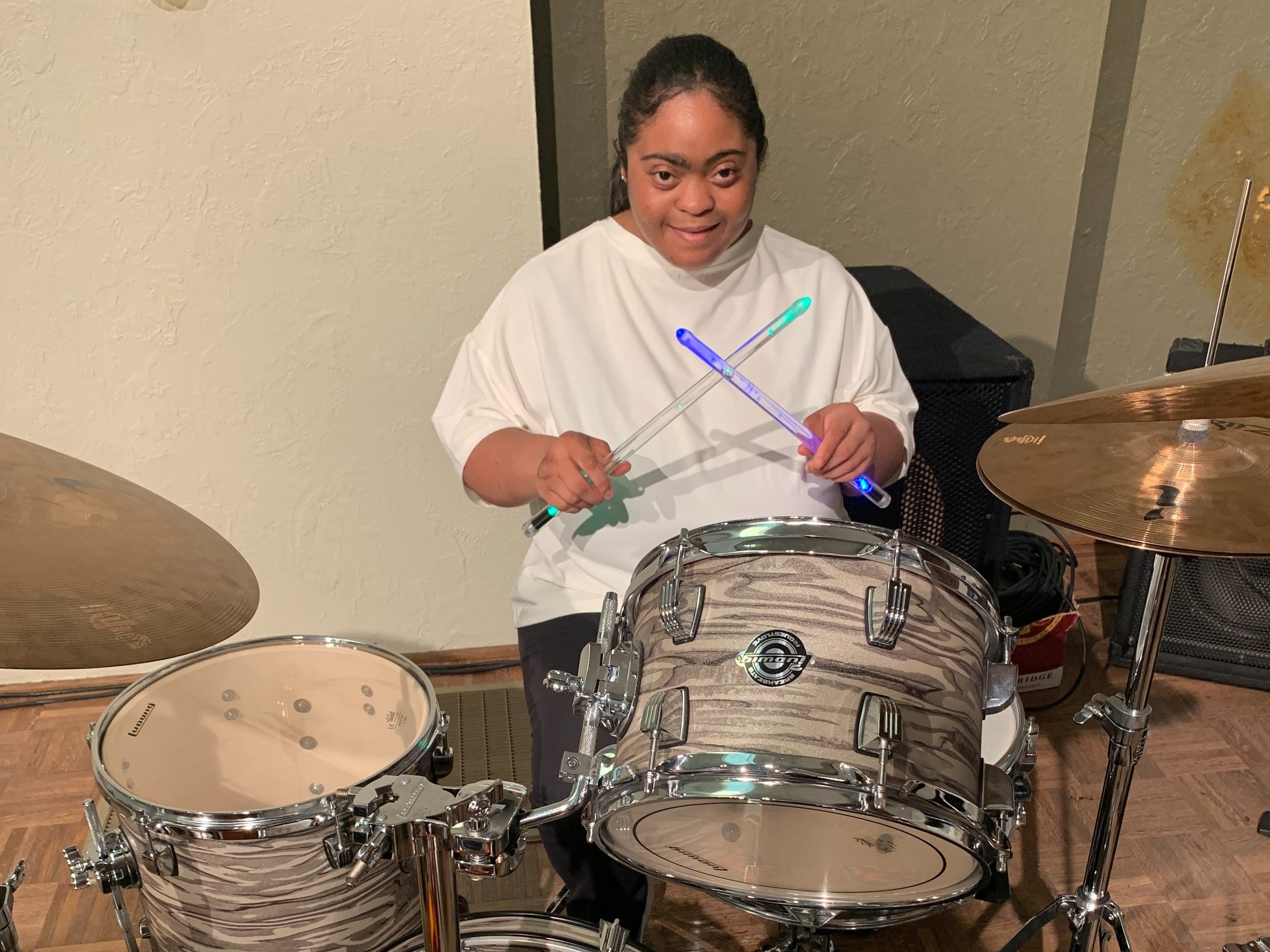  Creative Identity Anaheim participant Ashley smiling with her drum kit at the 2023 Summer Concert and Boutique called the “Coming Together as a Community” to an audience of attendees. 