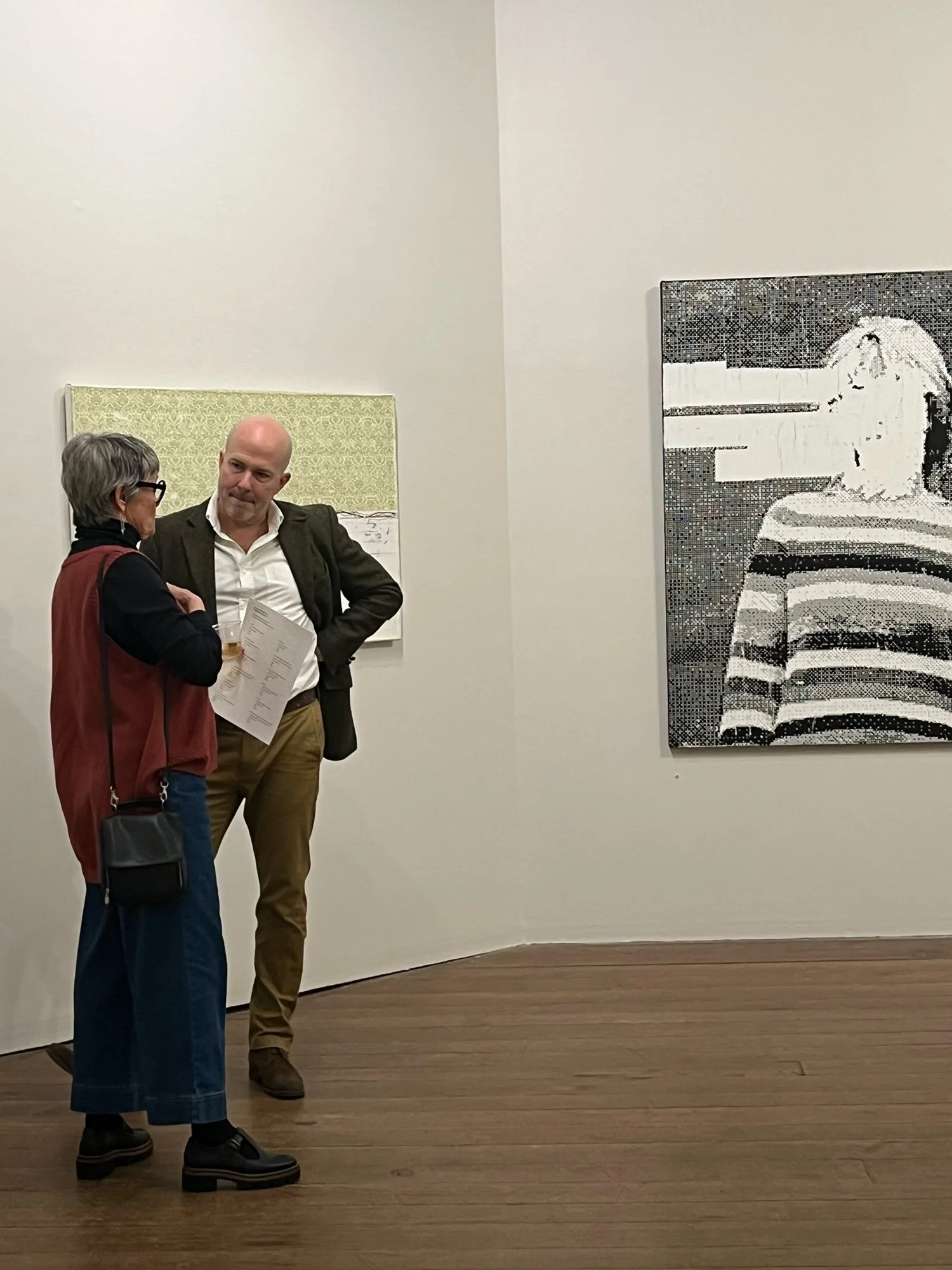 Two people engaging in a conversation inside an art gallery, with paintings on the wall behind them.
