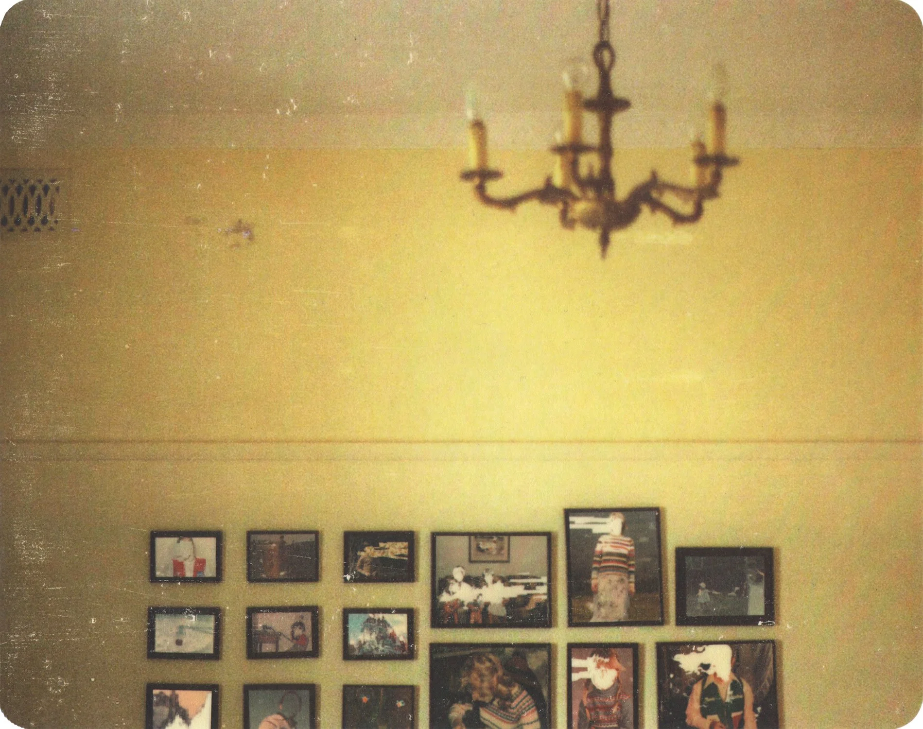 Hollis Brown Thornton pigment transfer of an empty yellow interior with a chandelier and a wall of framed family photographs containing partially erased and obscured figures.