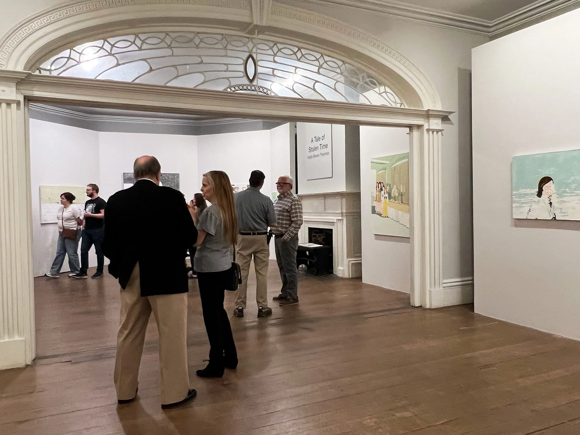 People viewing artwork in an art gallery with white walls and wooden floors.