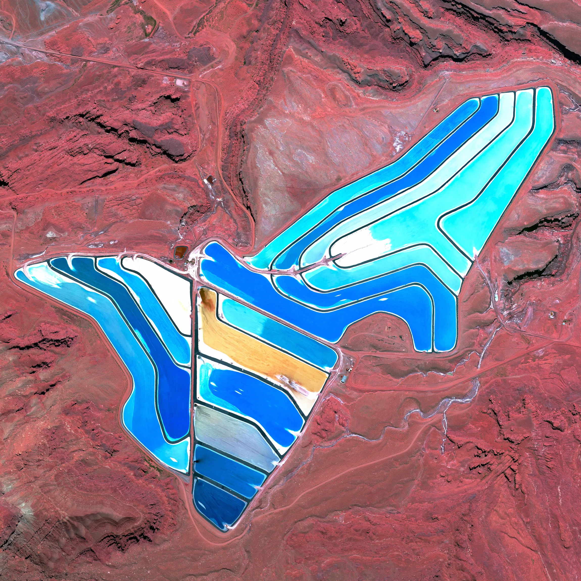 12/15/2015 Potash evaporation ponds Moab, Utah, USA 38.483377775°, -109.681333272° Blue evaporation ponds are visible at the Intrepid Potash Mine in Moab, Utah, USA. The mine produces muriate of potash, a potassium-containing salt used widely by farmers in fertilizer. The salt is pumped to the surface from underground brines and dried in massive solar ponds that vibrantly extend across the landscape. As the water evaporates over the course of 300 days, the salts crystallize out. So why are you seeing such vibrant colors? The water is dyed bright blue to reduce the amount of time it takes for the potash to crystallize; darker water absorbs more sunlight and heat.