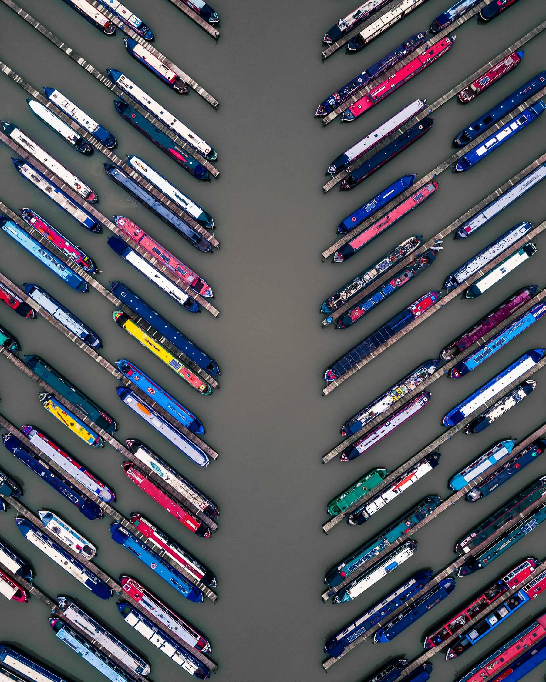 Colorful narrowboats are docked at Wigrams Turn Marina in Warwickshire County, England. These boats can be quite long, but are no more than 7 feet (2.13 meters) wide, allowing them to navigate narrow British canals. Thanks to restoration projects, much of England's 18th century canal system remains navigable today, used mostly for leisure boating. 52°15'26.4"N, 1°18'54.4"W Source imagery: Abstract Aerial Art