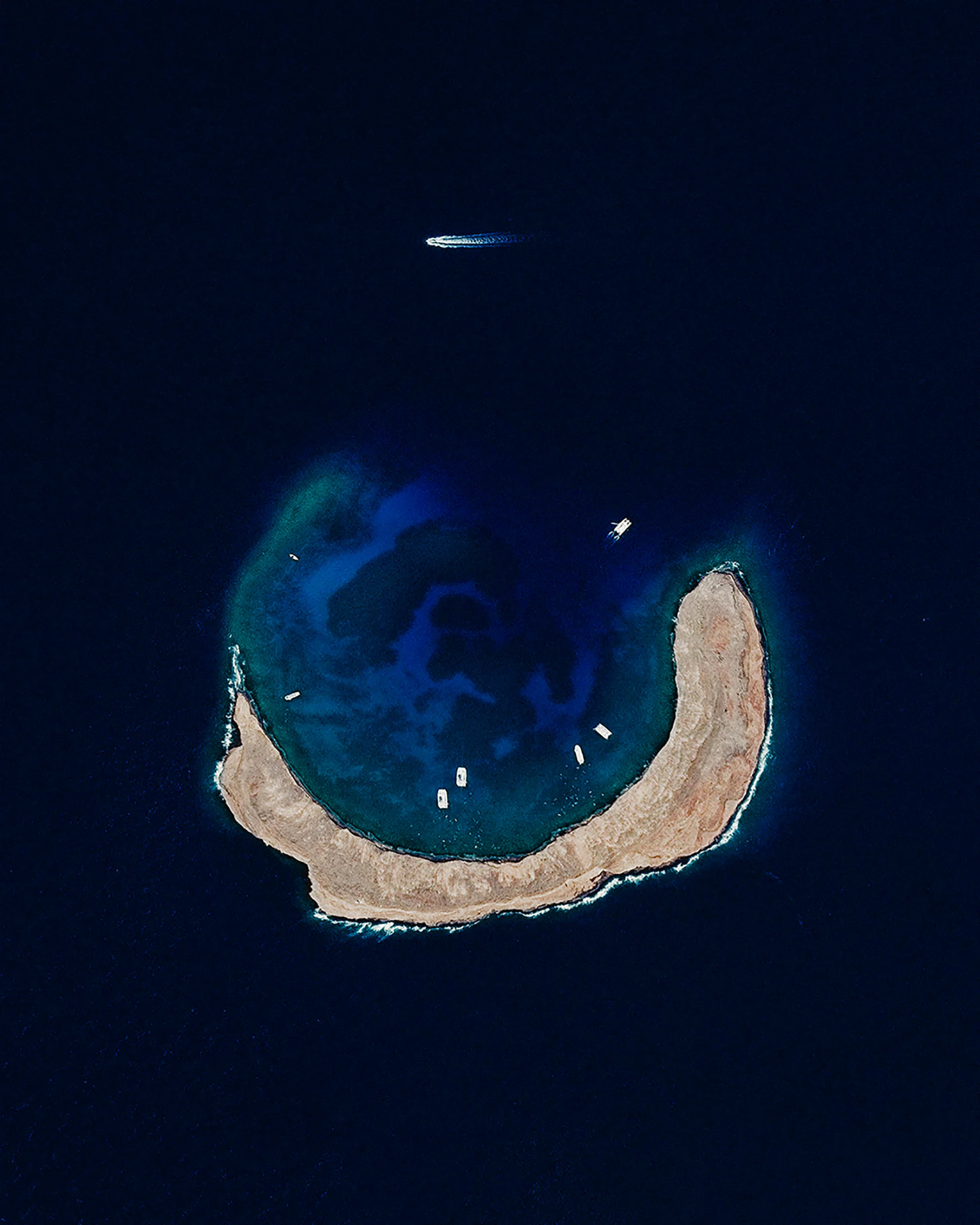Molokini is a small, uninhabited islet located between the Hawaiian Islands of Maui and Kahoolawe. It is formed by a crescent-shaped, partially submerged volcanic crater roughly 0.4 miles (0.6 km) in diameter. A lush reef inside the Molokini Crater is home to about 250 species of fish, making it a popular destination for scuba divers and snorkelers. 20°37'55.8"N, 156°29'46.2"W Source imagery: DigitalGlobe