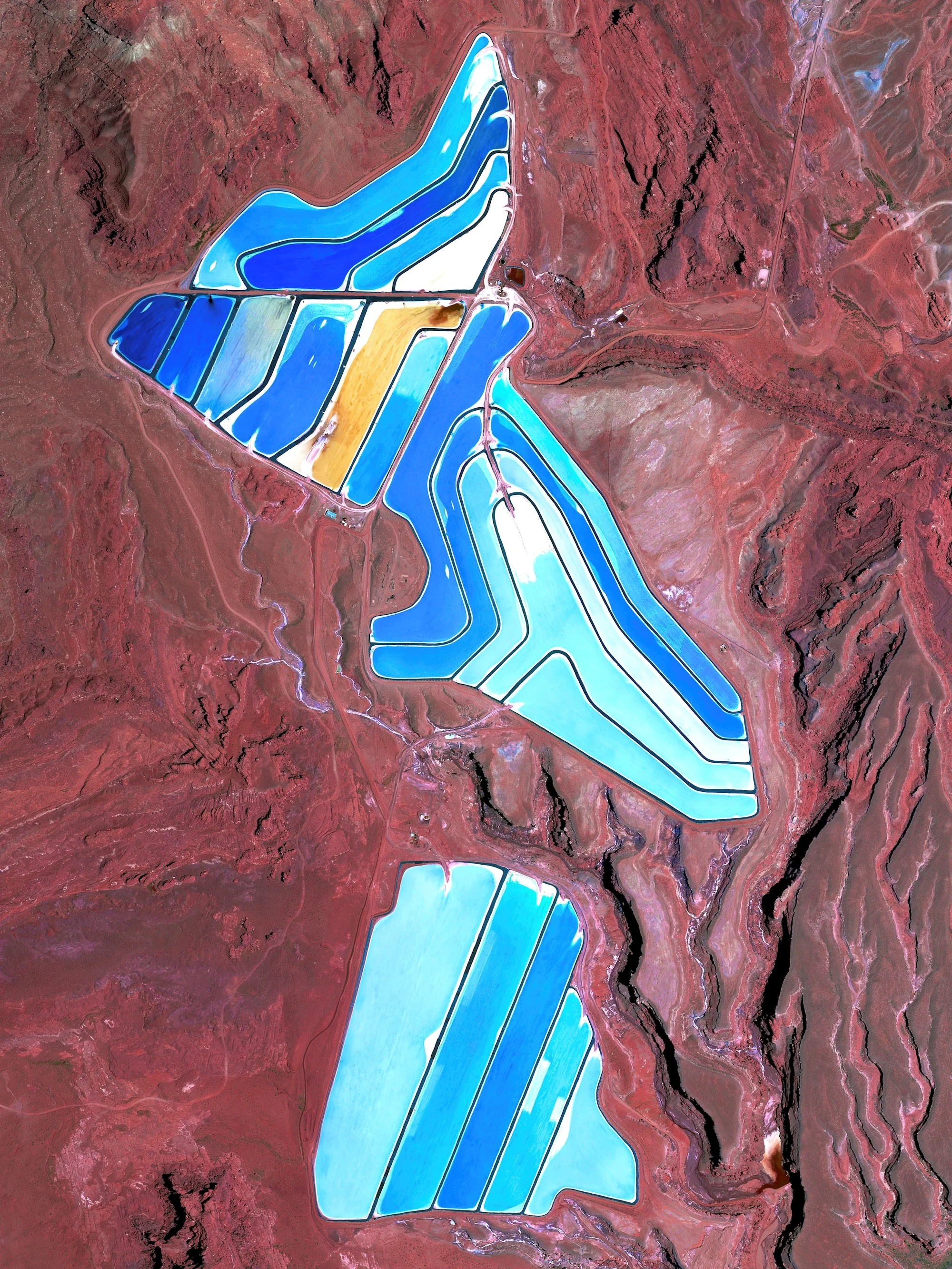 Evaporation ponds are visible at the Intrepid Potash Mine in Moab, Utah, USA. The mine produces muriate of potash, a potassium-containing salt that is a major component in fertilizers. The salt is pumped to the surface from underground brines and dried in massive solar ponds that vibrantly extend across the landscape. As the water evaporates over the course of 300 days, the salts crystallize out. The blue color seen here occurs because the water is dyed a deep blue to absorb more sunlight and heat, thereby reducing the amount of time it takes for the water to evaporate and the potash to crystallize. 38°29'08.1"N, 109°41'04.6"W Source imagery: DigitalGlobe