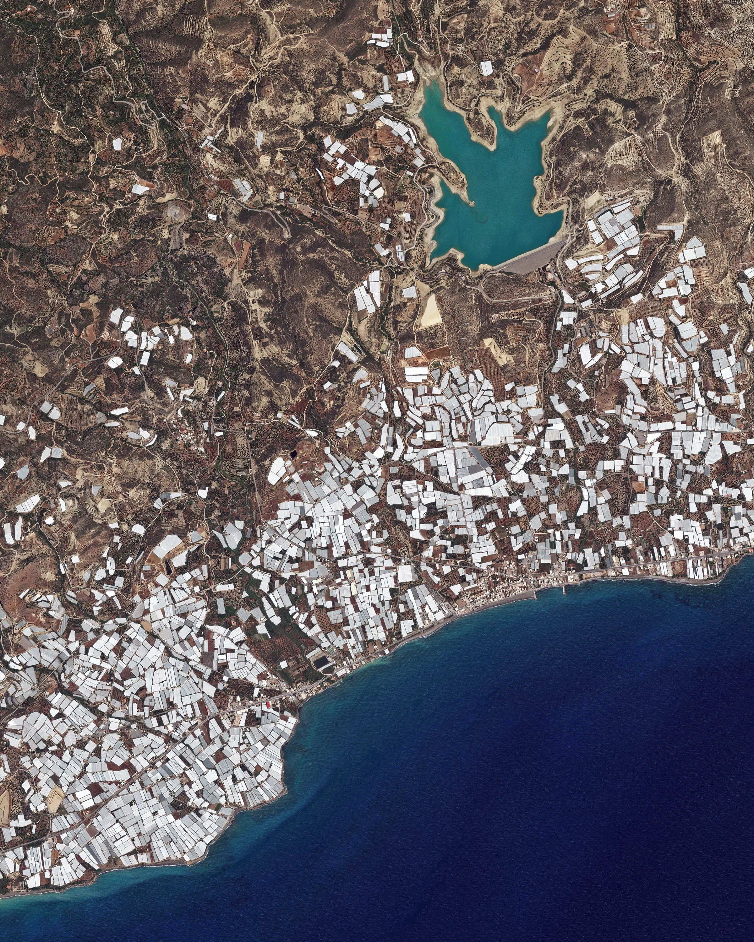 Plastic greenhouses cover a stretch of shoreline on the south coast of Crete — the largest and most populous of the Greek islands. Inside these greenhouses, which cover an area of roughly 6 square miles (15 sq. km), large quantities of fruits and vegetables are grown for export. In the upper right corner of this Overview is the Bramiana Reservoir, which was built in 1986 to meet the needs of the thousands of greenhouses surrounding it. 35°01'45.4"N, 25°41'46.0"E Source imagery: DigitalGlobe