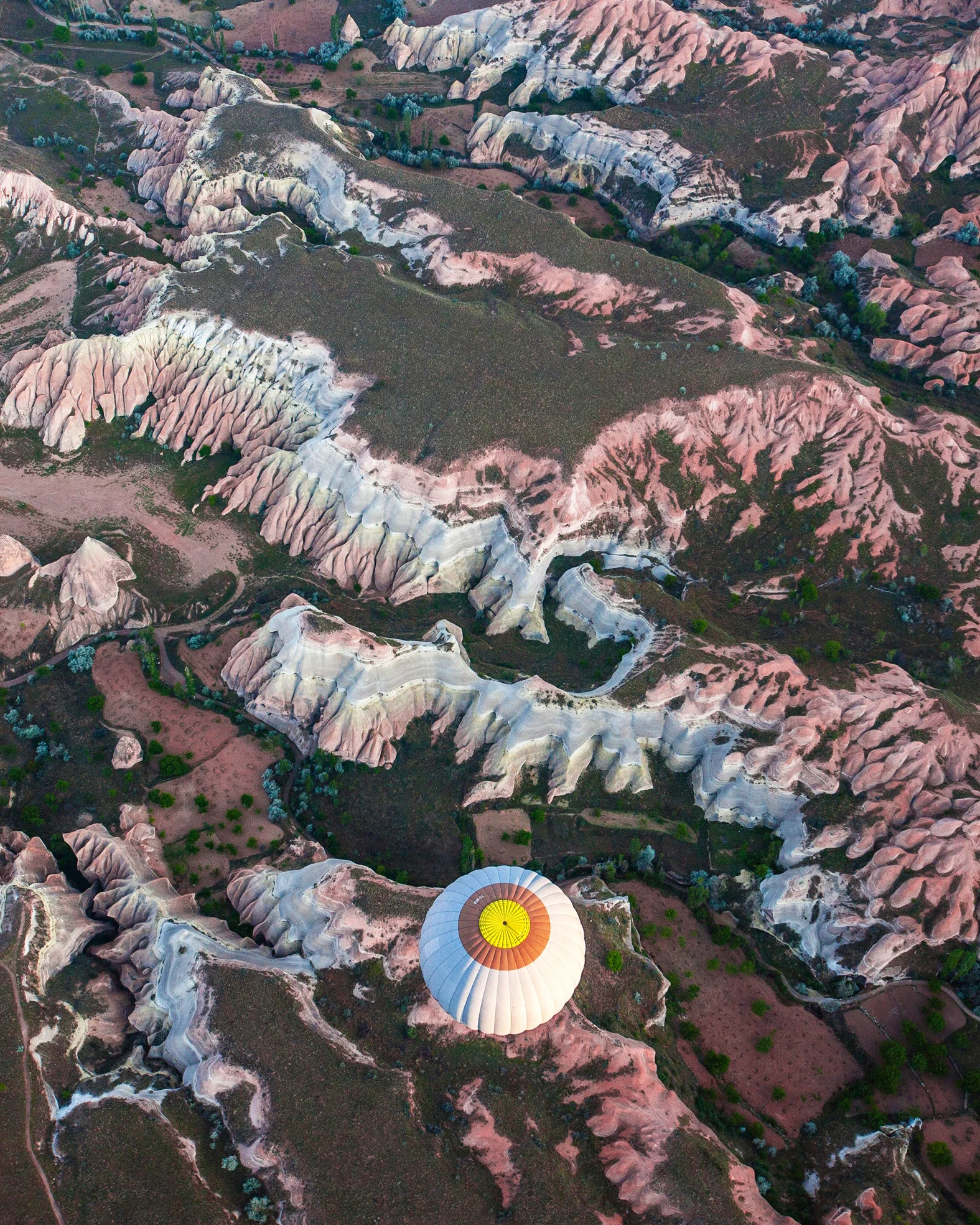 A hot-air balloon floats above Cappadocia, a historical region in Central Anatolia, Turkey. This semi-arid area is known for its distinctive "fairy chimneys" — tall, cone-shaped rock formations clustered across the landscape. Hot-air ballooning is very popular in Cappadocia and is available to tourists in Göreme, a local town. 38°38'35.0"N, 34°49'44.0"E Source imagery: Mahir Uysal