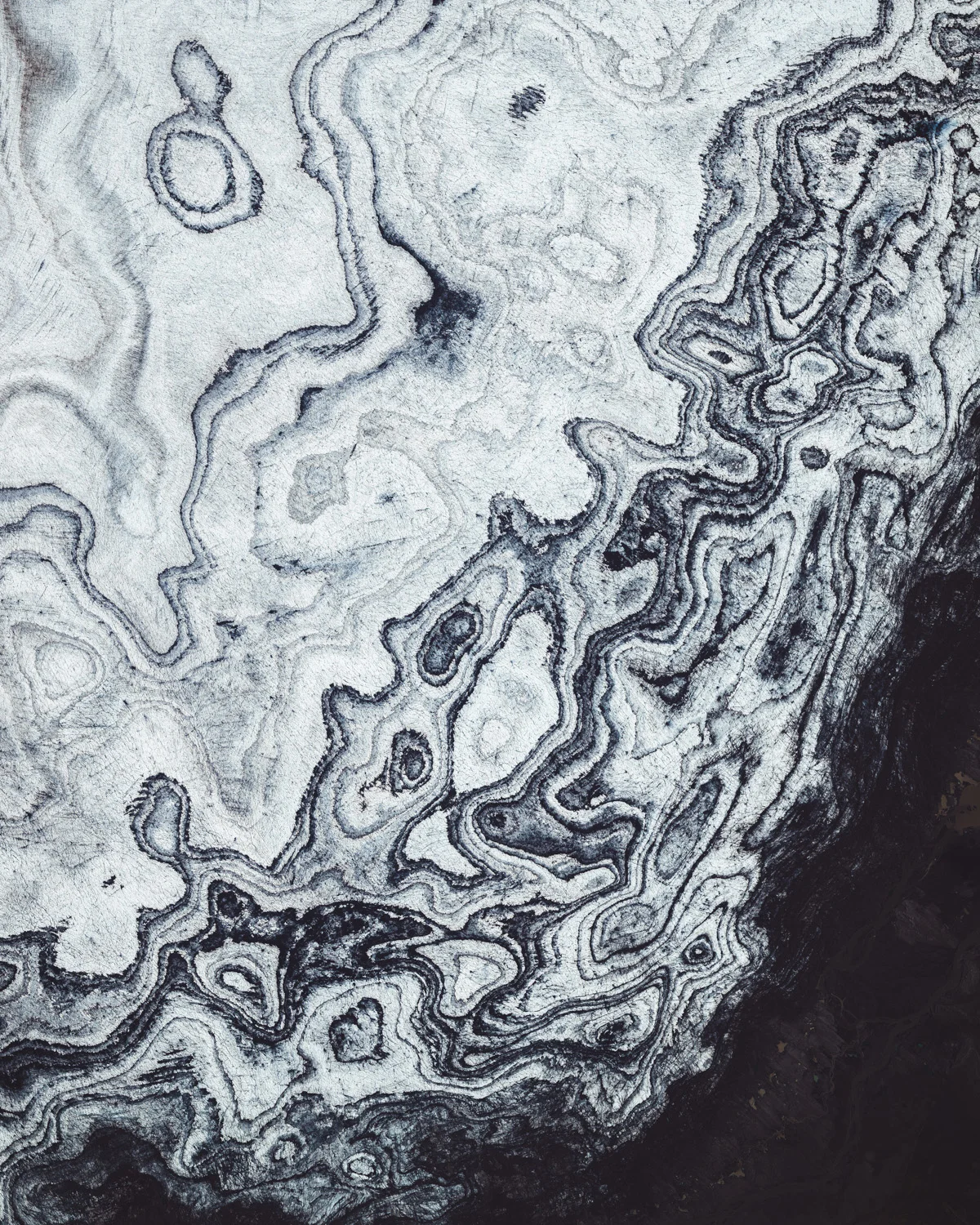 Glacial ice and volcanic sediment form contrasting patterns along the southwestern rim of Vatnajökull Glacier in Iceland. Vatnajökull is the largest and most voluminous ice cap in Iceland, covering an area of 3,100 square miles (7,900 square km) — roughly 8% of the country's total landmass. Underneath it are several volcanoes, many of which continue to erupt and can burst weakened ice, leading to glacial lake outburst floods and landslides. 64.130241°, -17.978260° Source imagery: Maxar Technologies