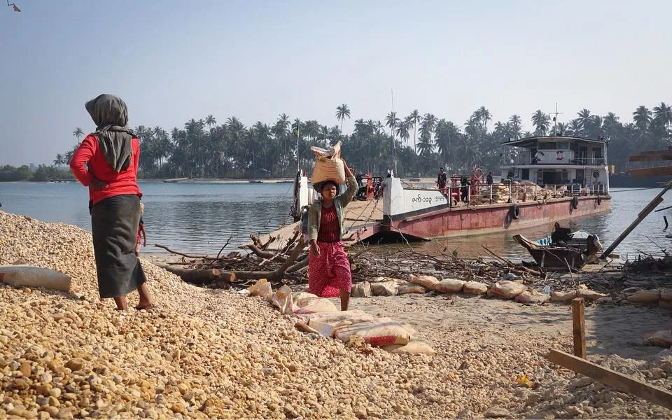 Men and women carry rocks from the river to the mainland, where a bridge is being constructed. Feb 2018.