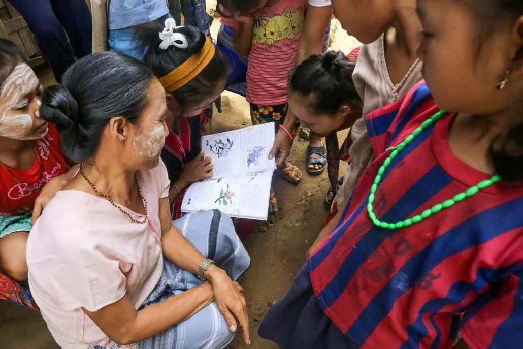 Women in a Karen IDP read through a newly released report on orchids.