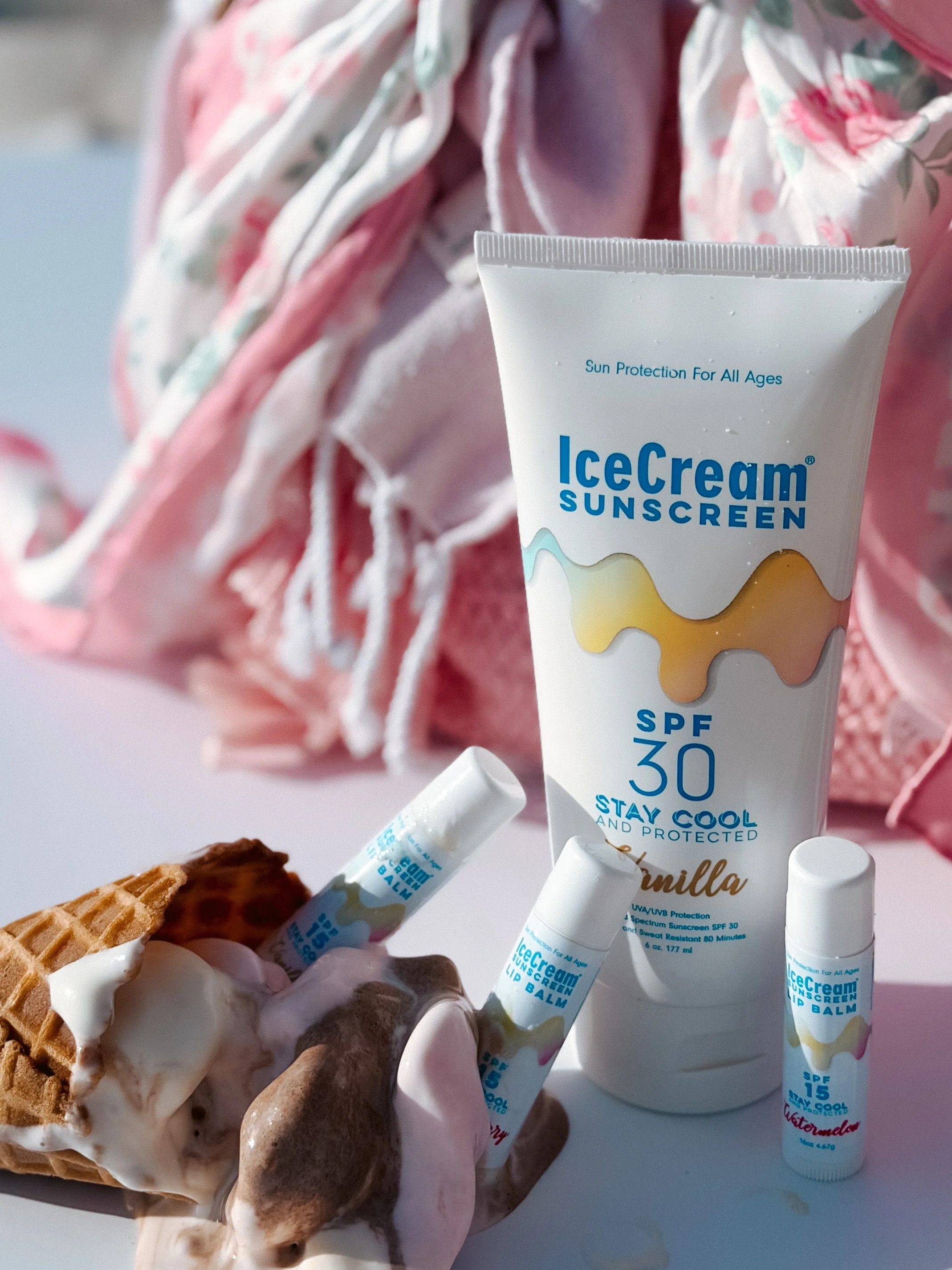 A container of IceCream Sunscreen SPF 30 with vanilla scent, two lip balms, and melting ice cream on a waffle cone.