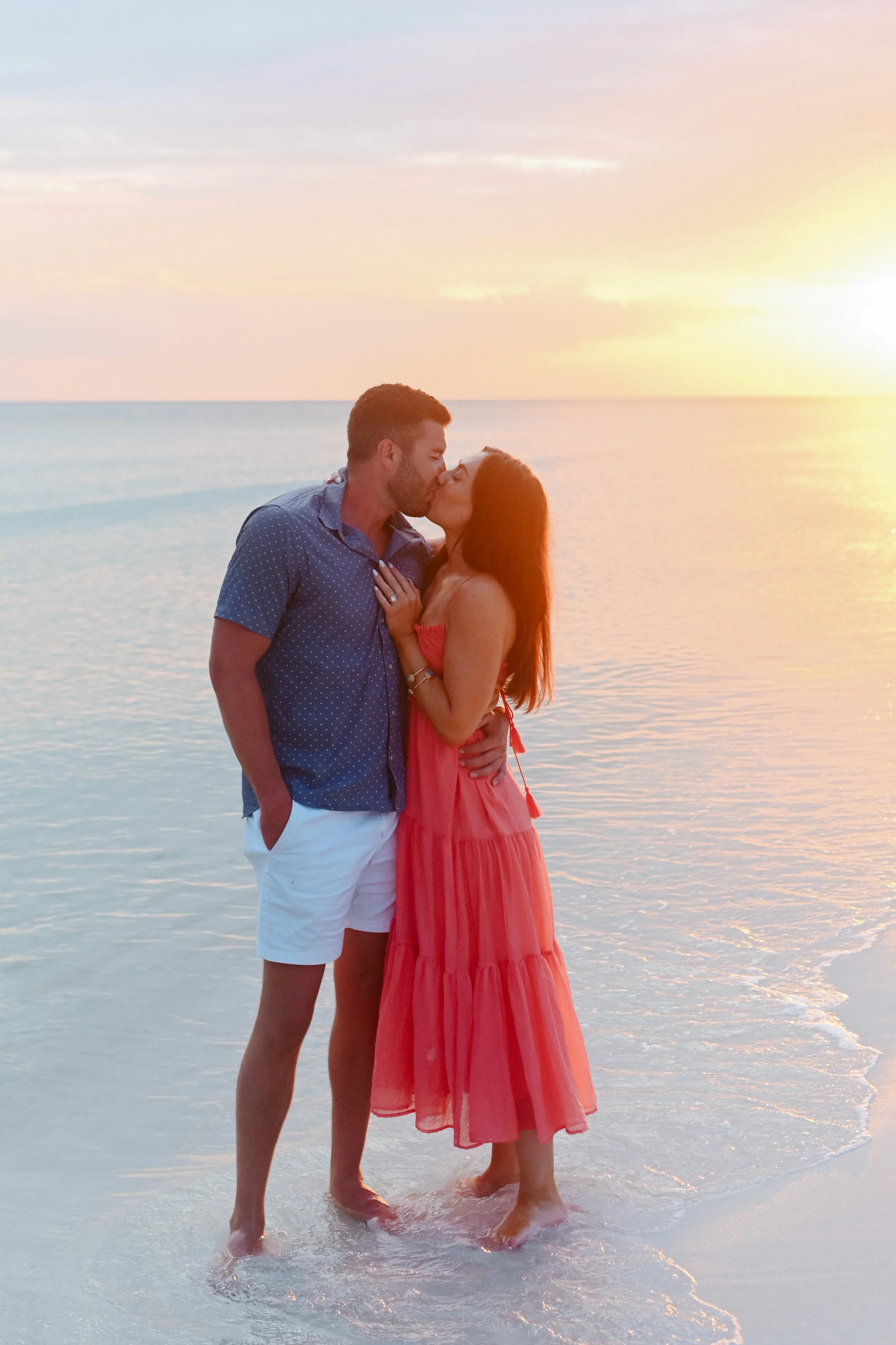 A couple kissing on the beach at sunset with the ocean in the background.