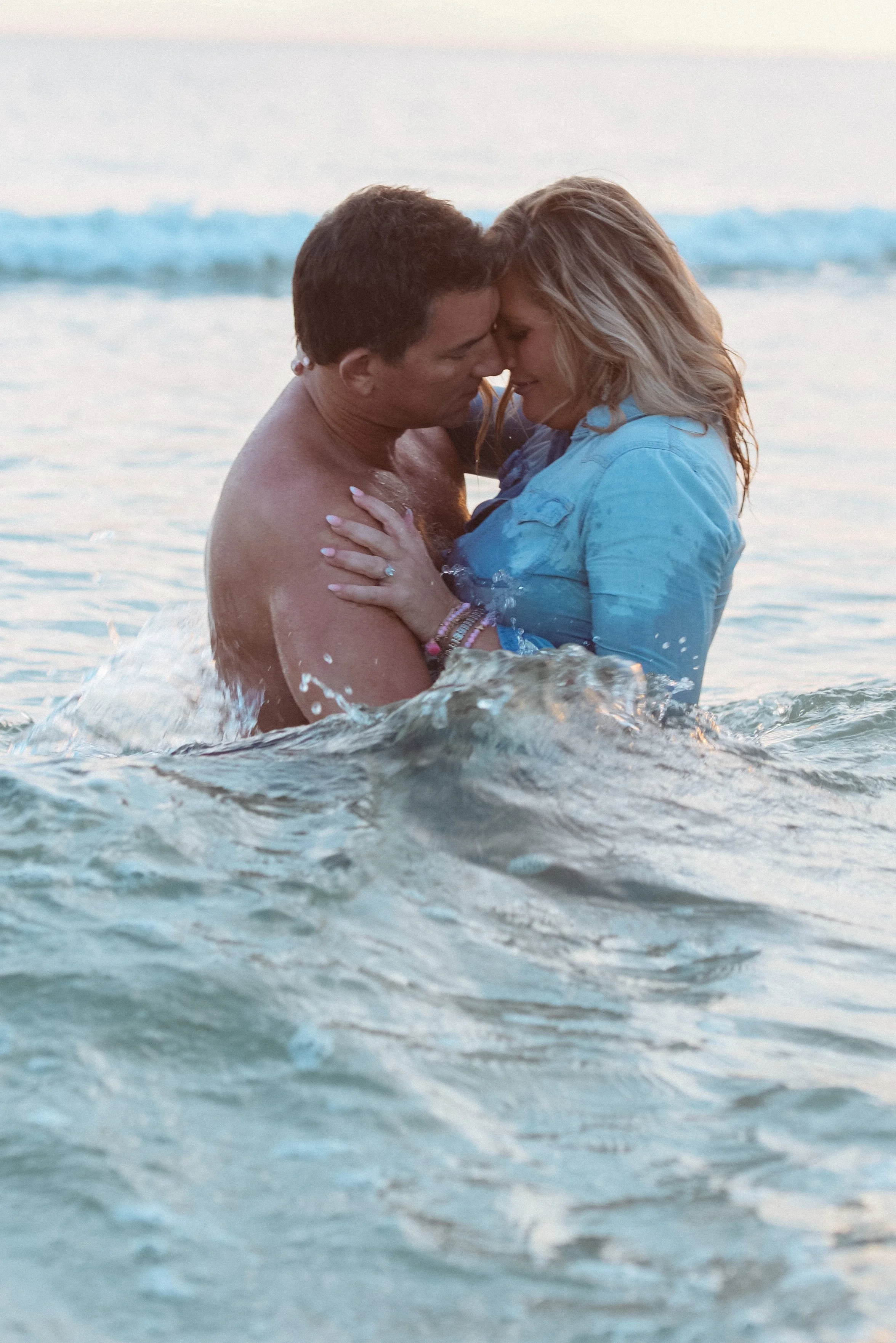 A couple embracing in the ocean, touching foreheads, during sunset.