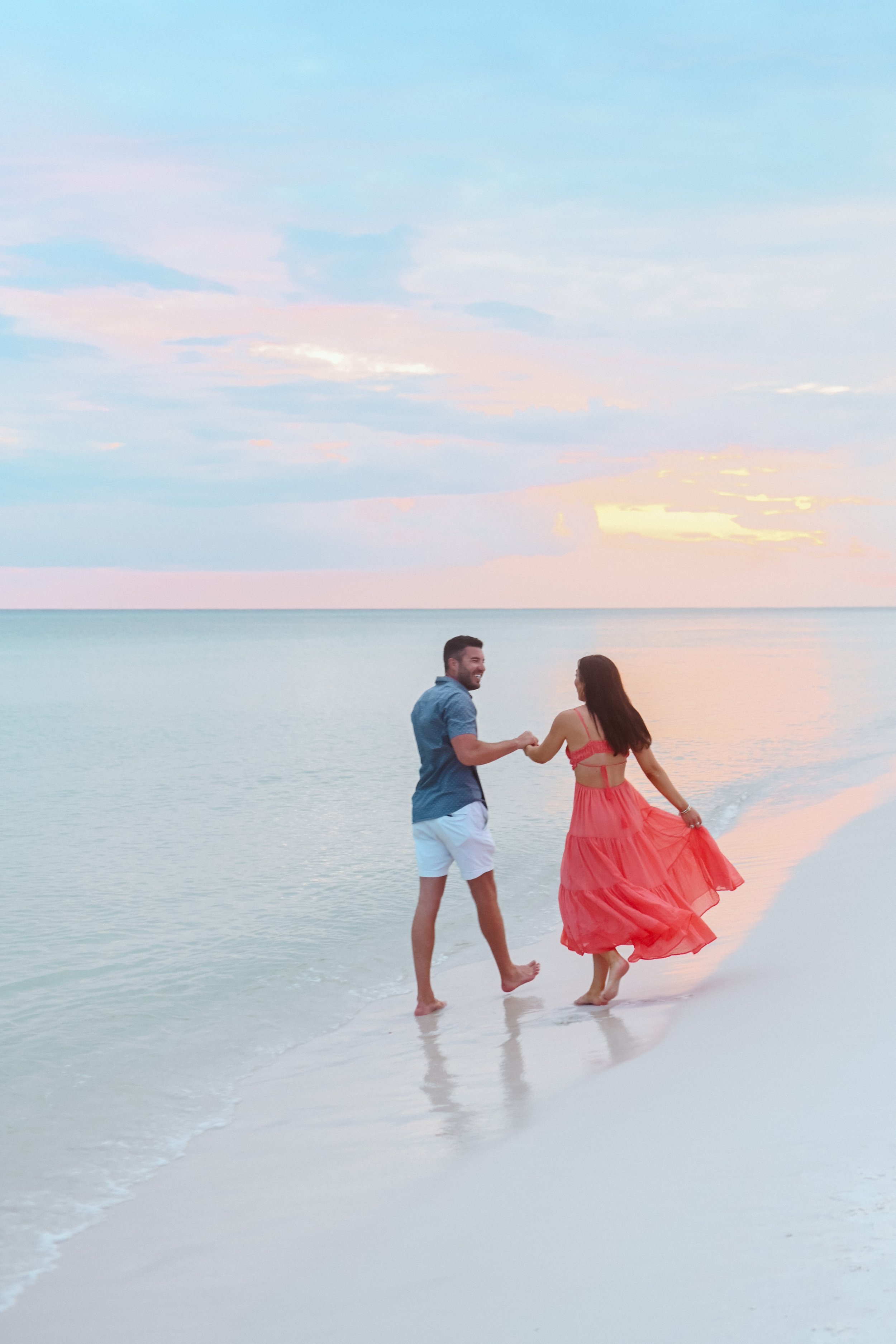 A couple dancing on the beach at sunset, holding hands and smiling.