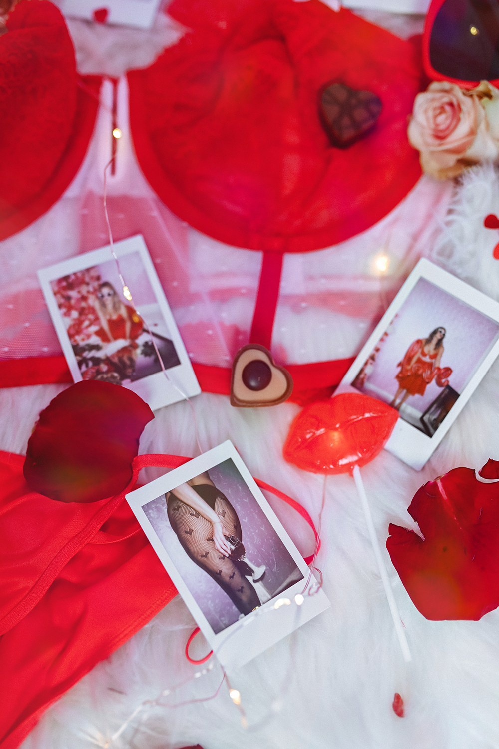 Valentine's Day display with a large red heart-shaped object, roses, photos of a woman in lingerie, red lips, and heart-shaped decorations, illuminated with fairy lights.