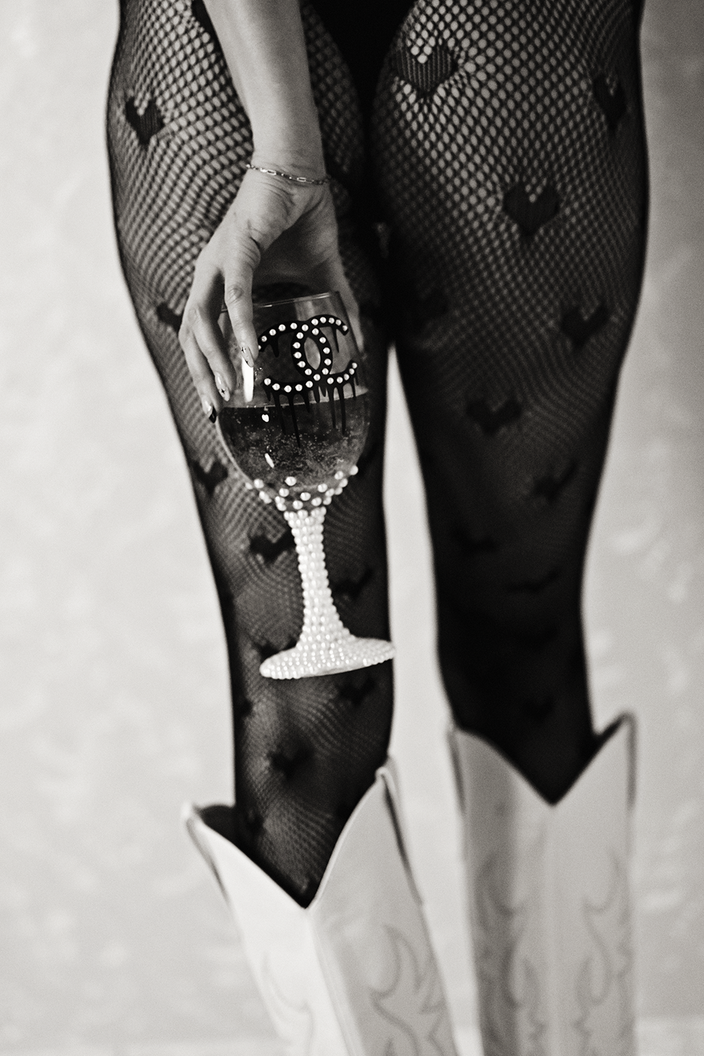 A woman wearing fishnet stockings with heart patterns, holding a wine glass with the Chanel logo, and wearing high-heeled boots.