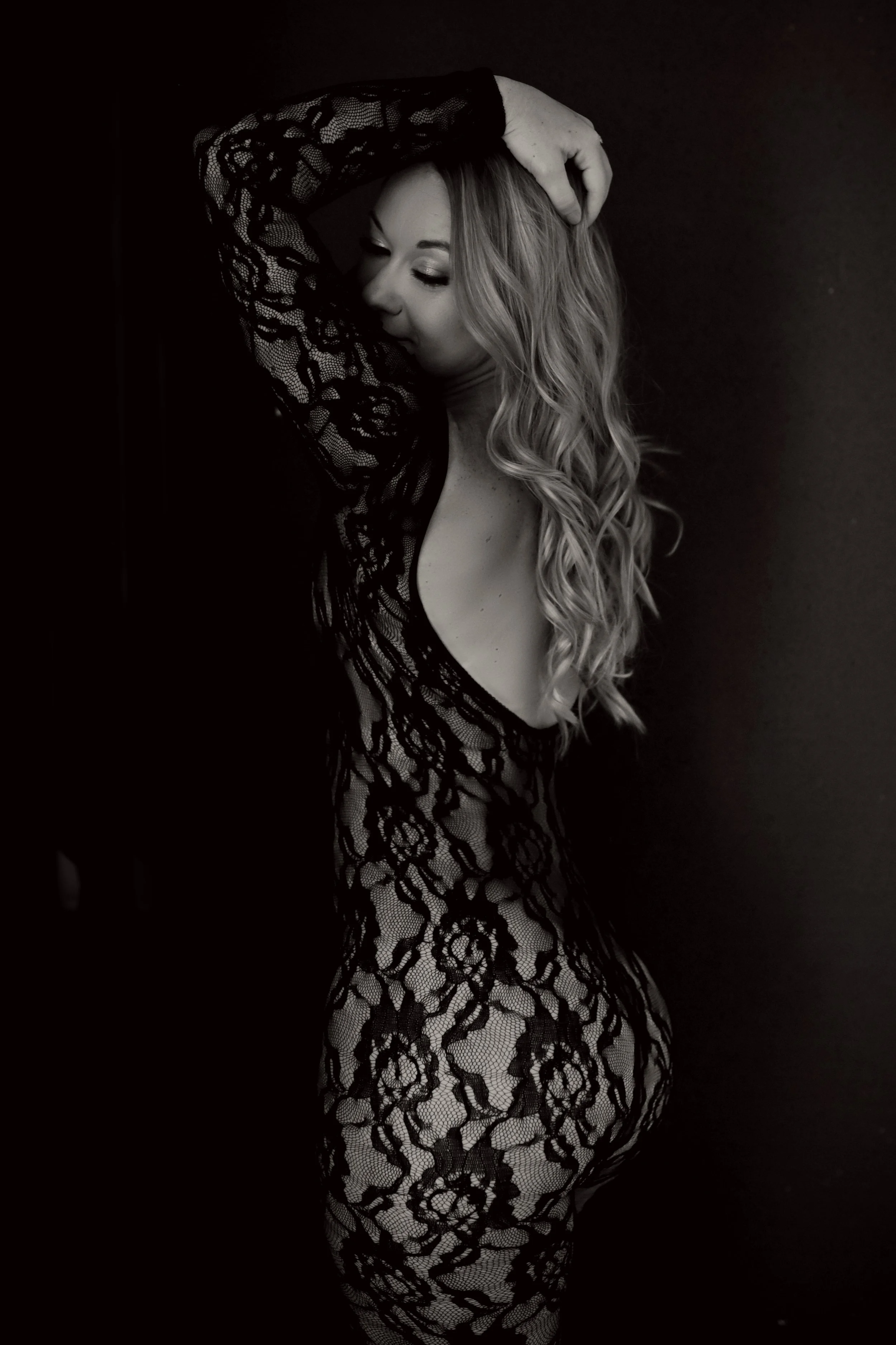 A woman with long, wavy hair wearing a black lace dress standing against a dark background.
