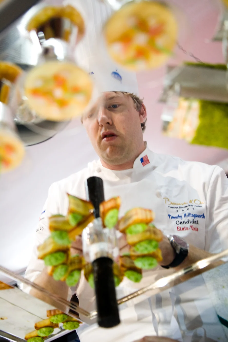 Pendant que le plat de poisson de l'équipe précédente est dégusté par le jury, le chef de l'équipe américaine, Timothy Hollingsworth finit la mise en place de son plat de viande.