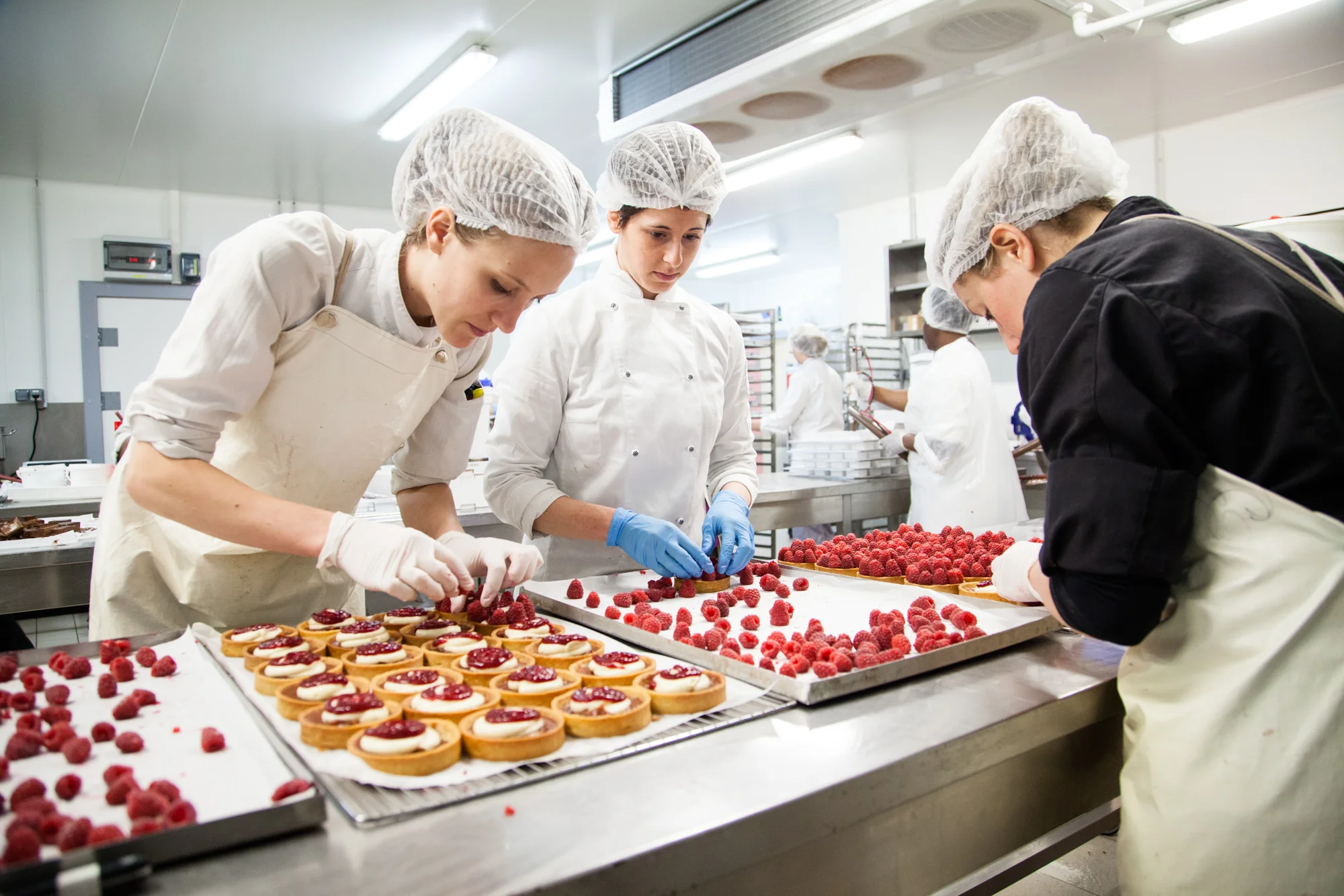 Dans le laboratoire de production, des pâtissières élaborent des tartes à la framboise.