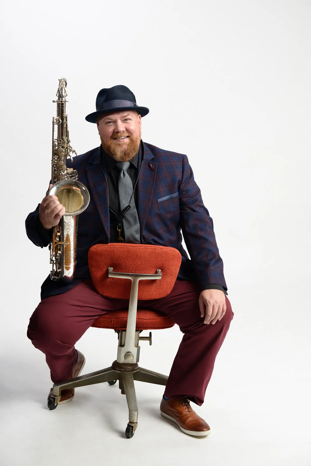 Matt Parker seated on a vintage office chair, holding his tenor saxophone