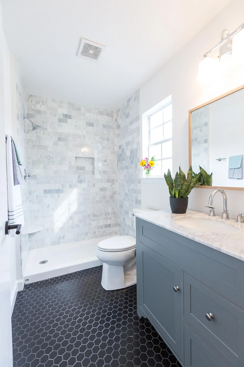 Carrara Marble tile shower surround. Black hex tile. Gray vanity with Carrara marble top, wide spread faucet. White Oak mirror, Milan hardware. 