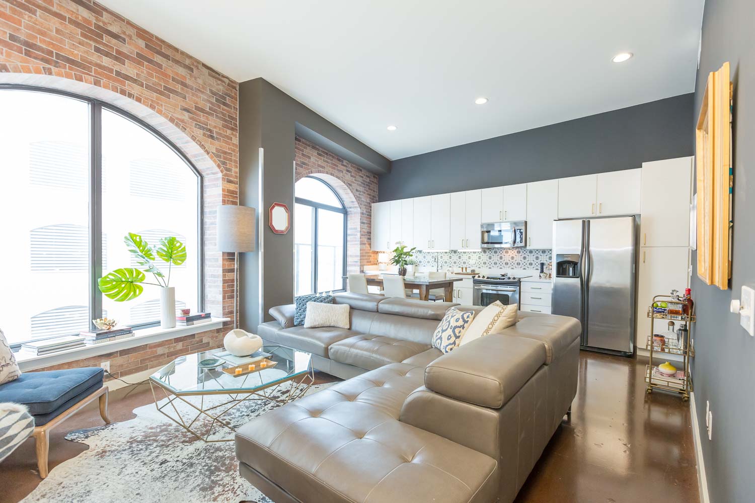 After - We added the brick at the arched windows and selected Sherwin Williams Deep Spacethe walls. The cabinets were painted white and gold hardware was added. The stained concrete floors were complimented with the cowhide rug. We worked with the existing taupe leather sofa. 