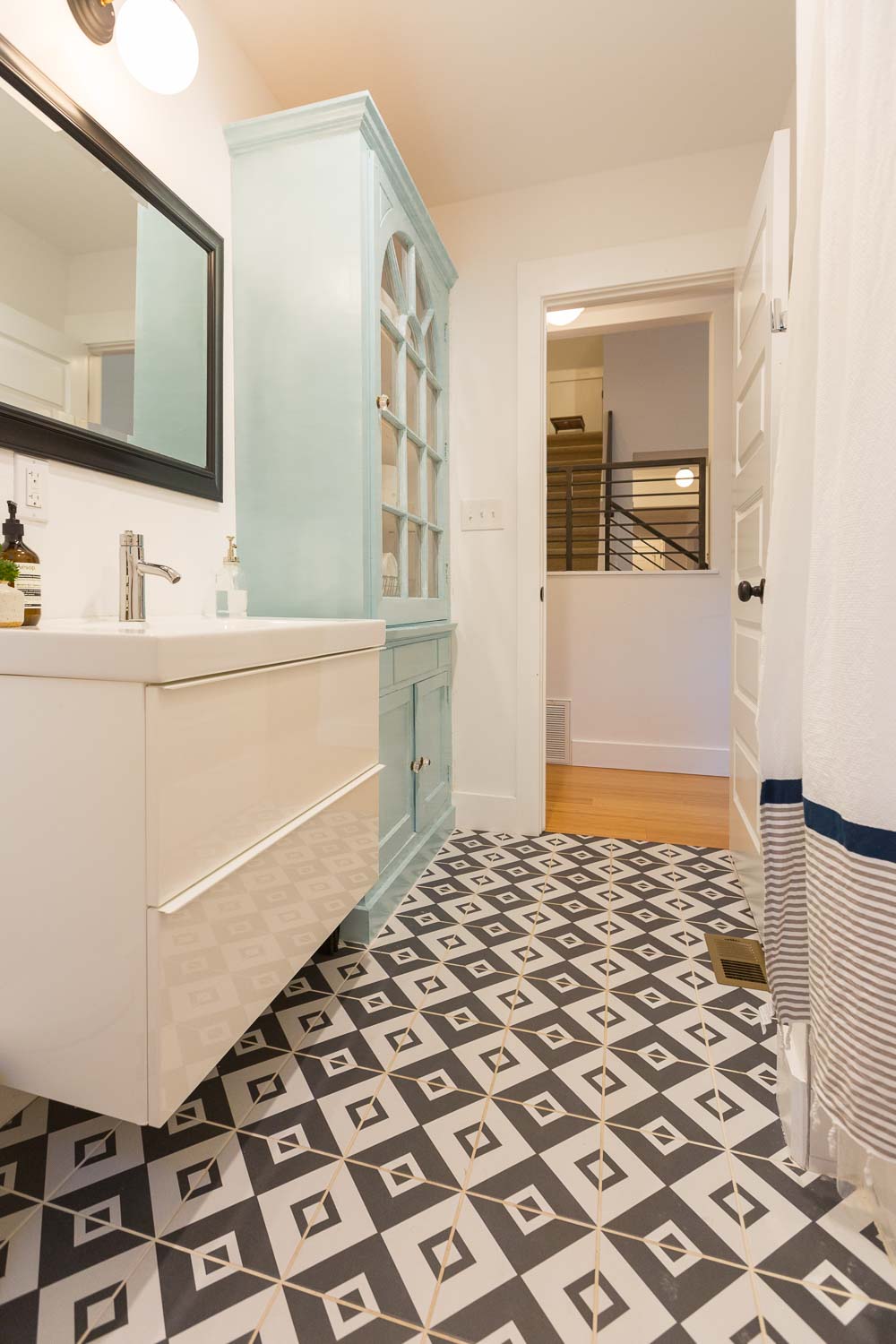 We love the guest bathroom with the bold black and white tile patterned floor. We reused the original dining room hutch as a linen cabinet. It sings in a soft aqua color. The modern ikea vanity was an affordable addition.