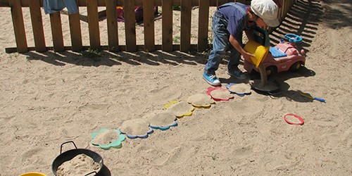 Una niña juega en el arenero rellenando moldes con arena.