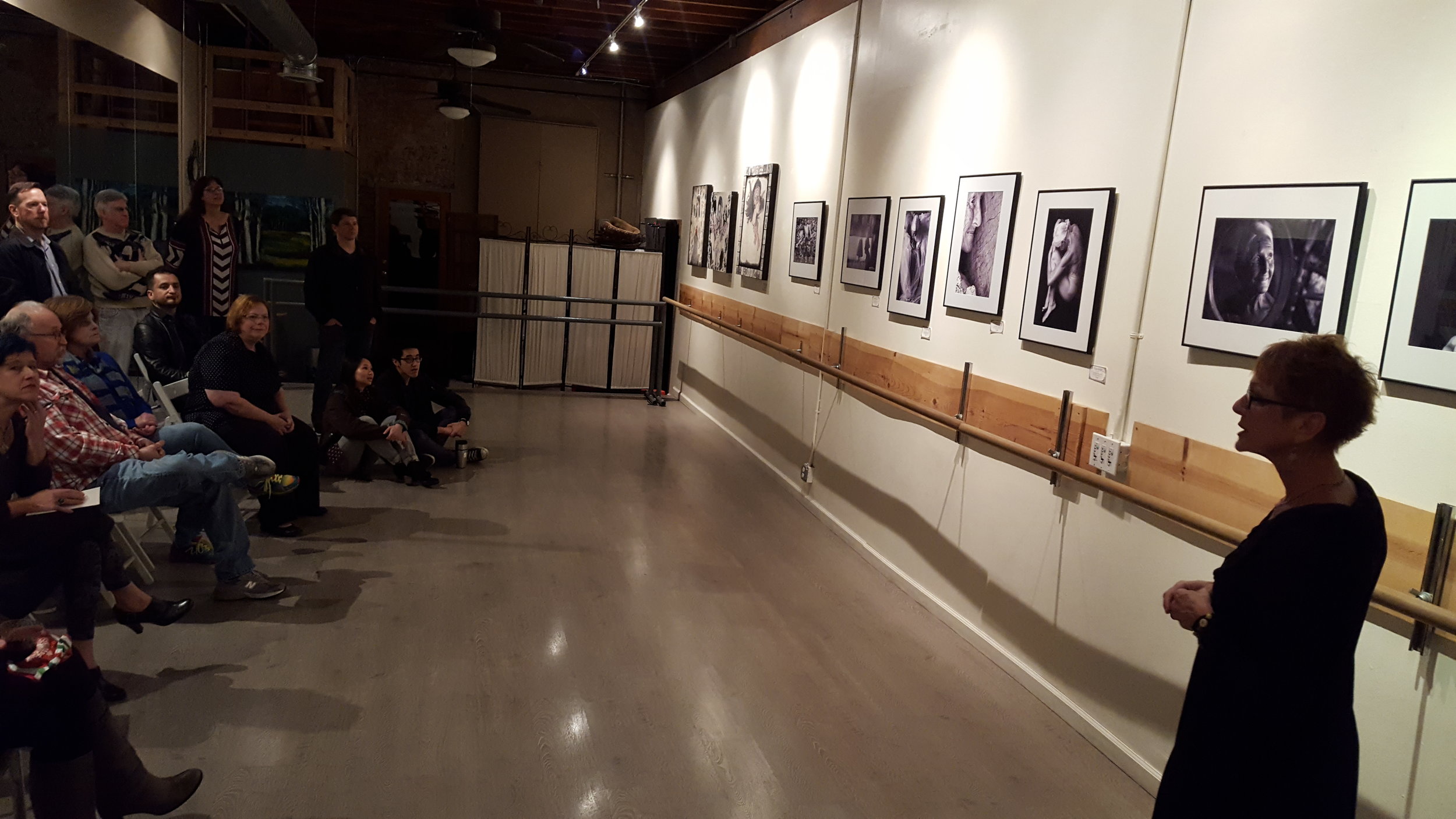 Mara Zaslove speaking in front of her black and white photographs. 